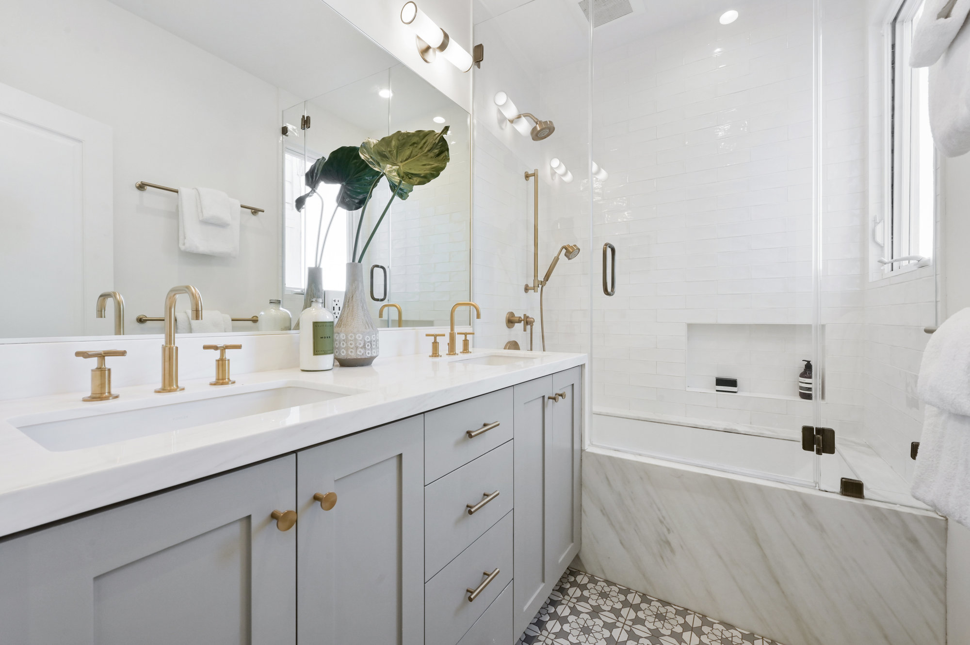 Bathroom with light grey cabinets and gold fixtures, featuring a bath with a glass door