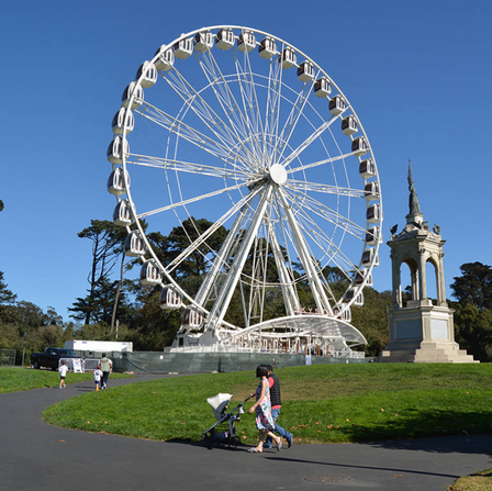 Two people push a stroller near a ferris wheel