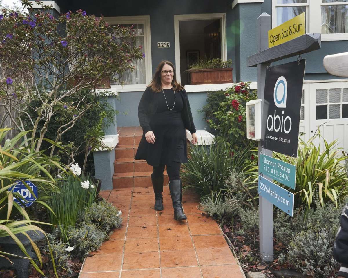 A person walking out of a house with a for sale sign