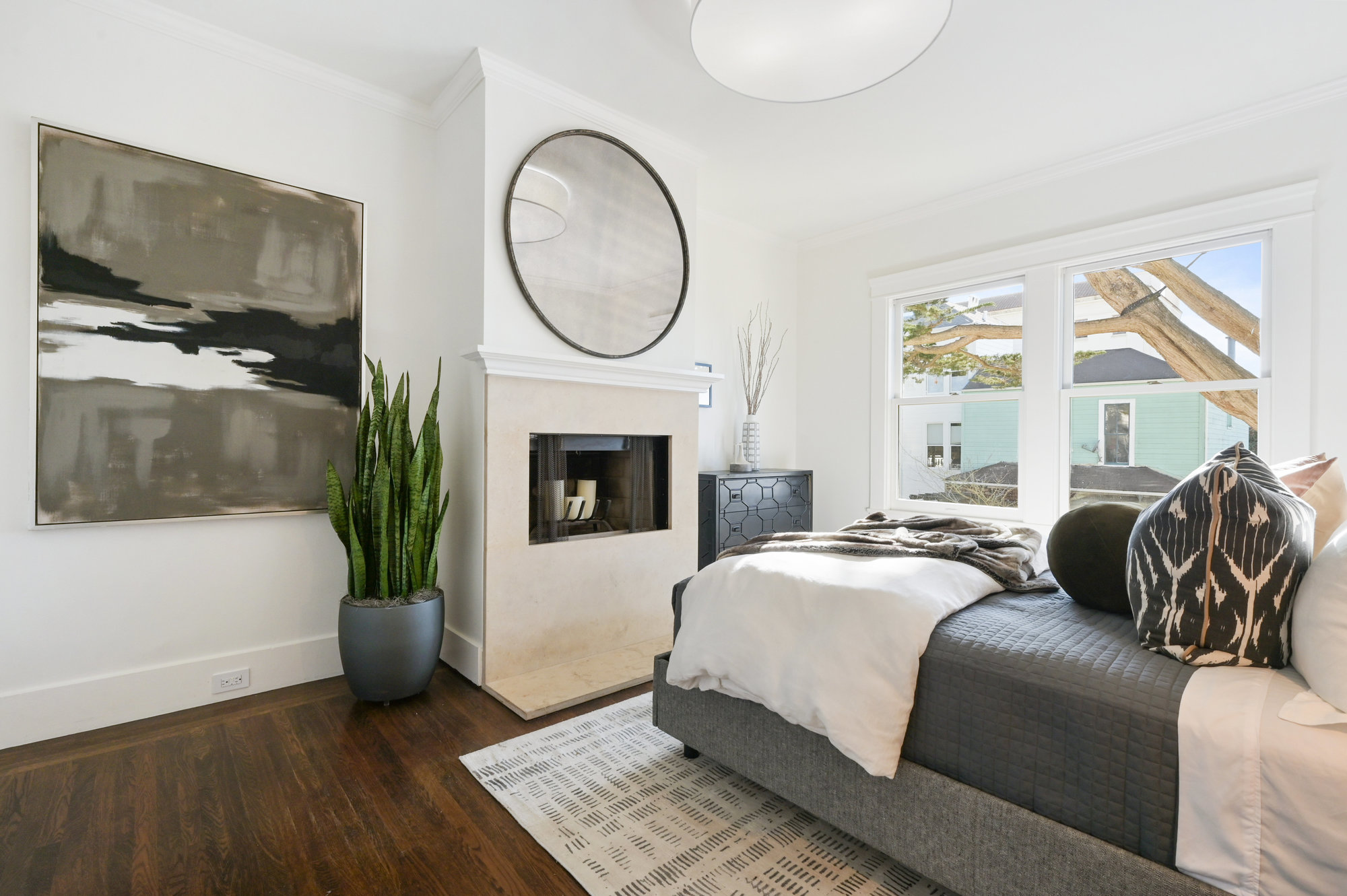 View of the primary bedroom, featuring large windows, a fireplace and wood floors