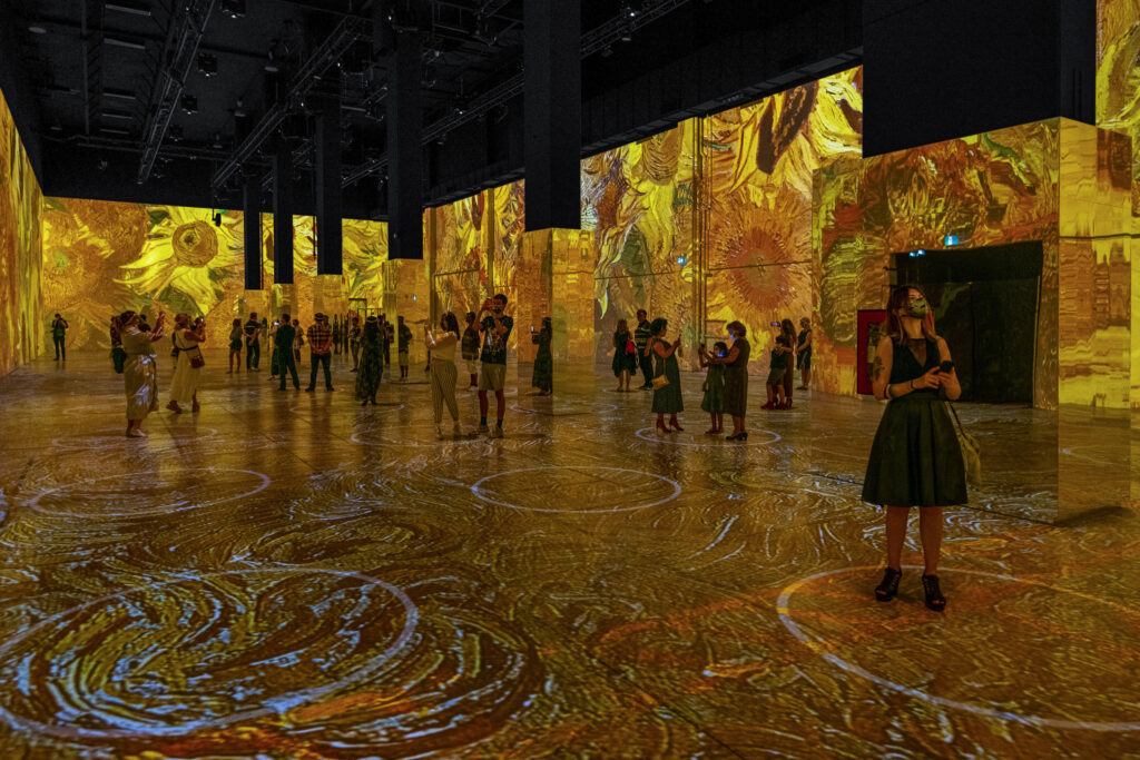 People standing in a room looking at the walls which are covered in art by Van Gogh’s