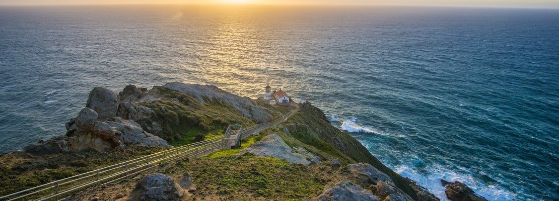 A view of the ocean with a lighthouse at the edge of a cliff