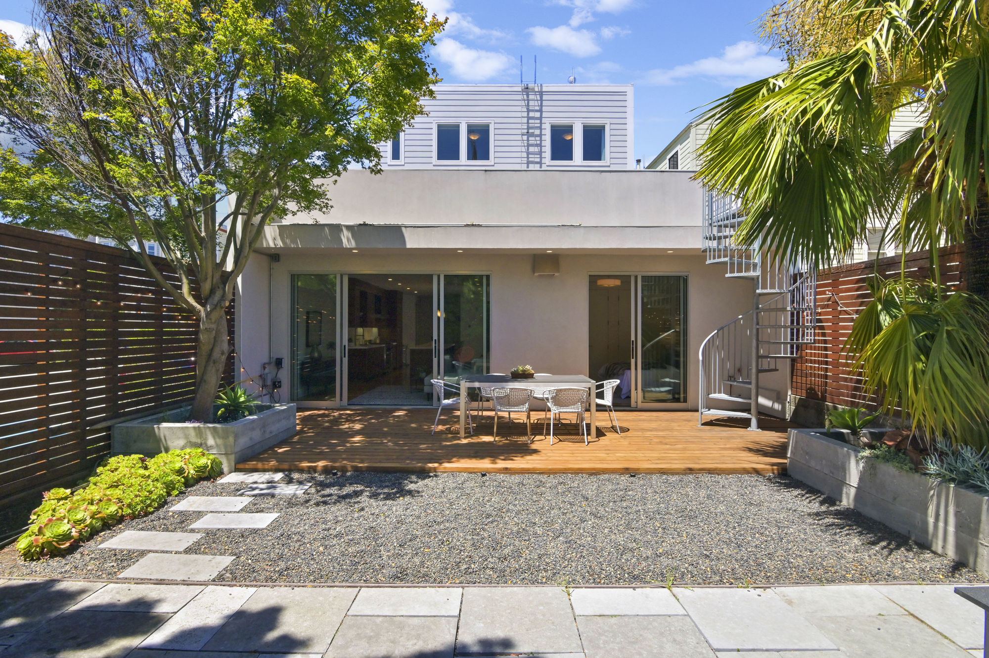 Property Photo: Rear exterior view of the ground-level outdoor space, showing an outdoor living area and palm trees