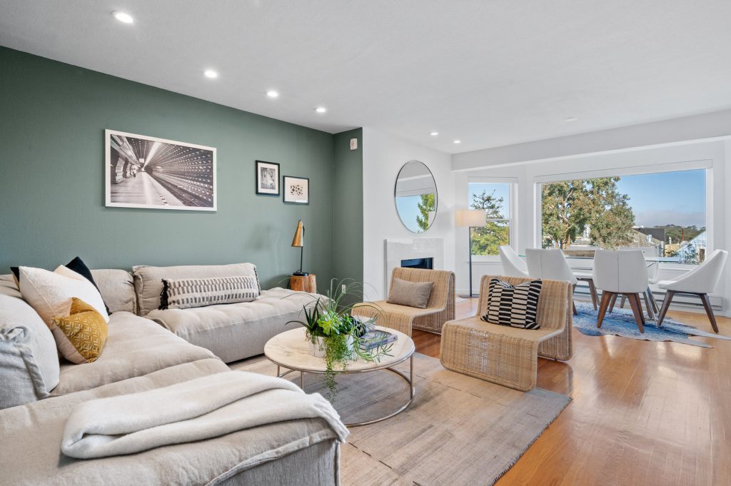 Living/dining space of 222 Parnassus Unit E. Open concept w/ large L shaped couch and dining table in front of windows looking out to backyard.