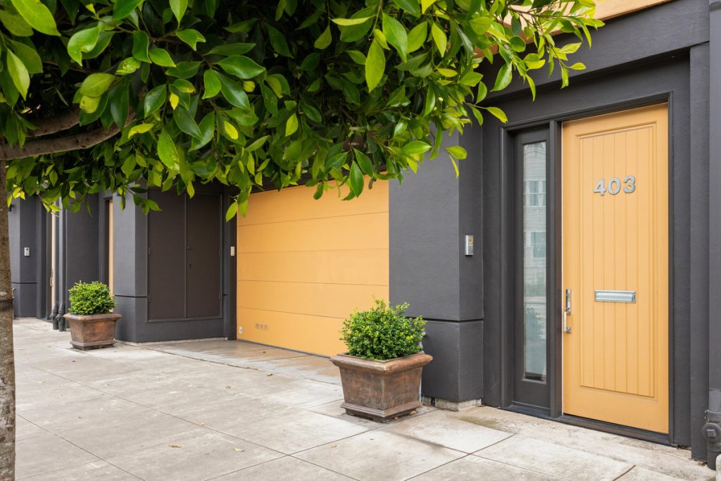 Front and garage door of 403 Carl street. Tree in front of building adds some greenery and there are bushes on both side of garage.