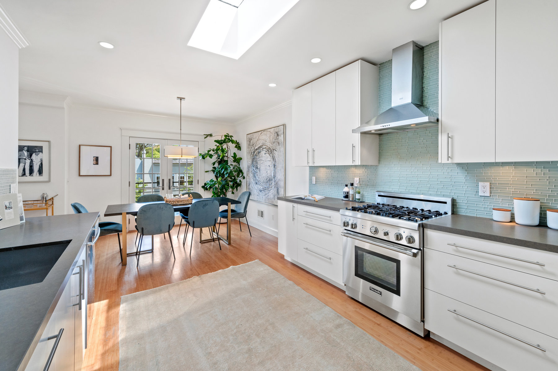 Looking towards dining from kitchen. Gas stainless stove with hood to the right with light blue tile backsplash.