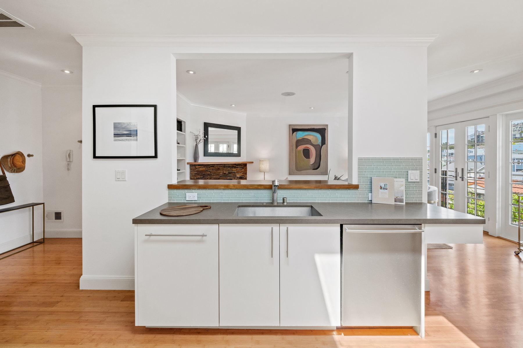Photo has kitchen sink centered. There is cut out in wall above sink that looks into living room.