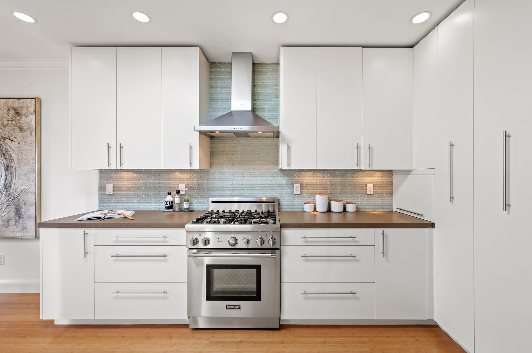Photo with kitchen stove centered. Stove has matching stainless hood.  There are upper and lower cabinets on both sides of stove.