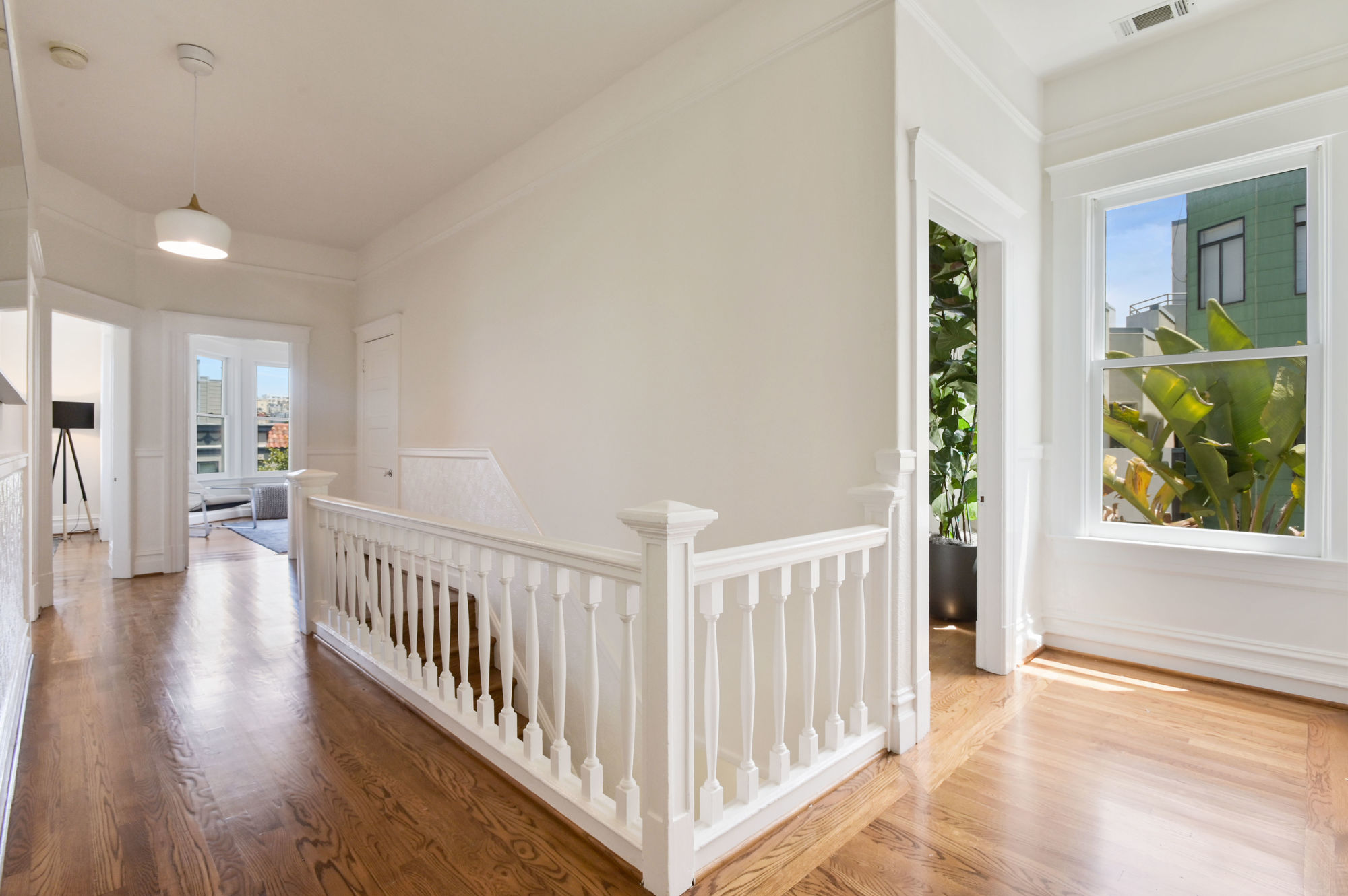 View of the sun-lit hallway, featuring white railing for steps leading down
