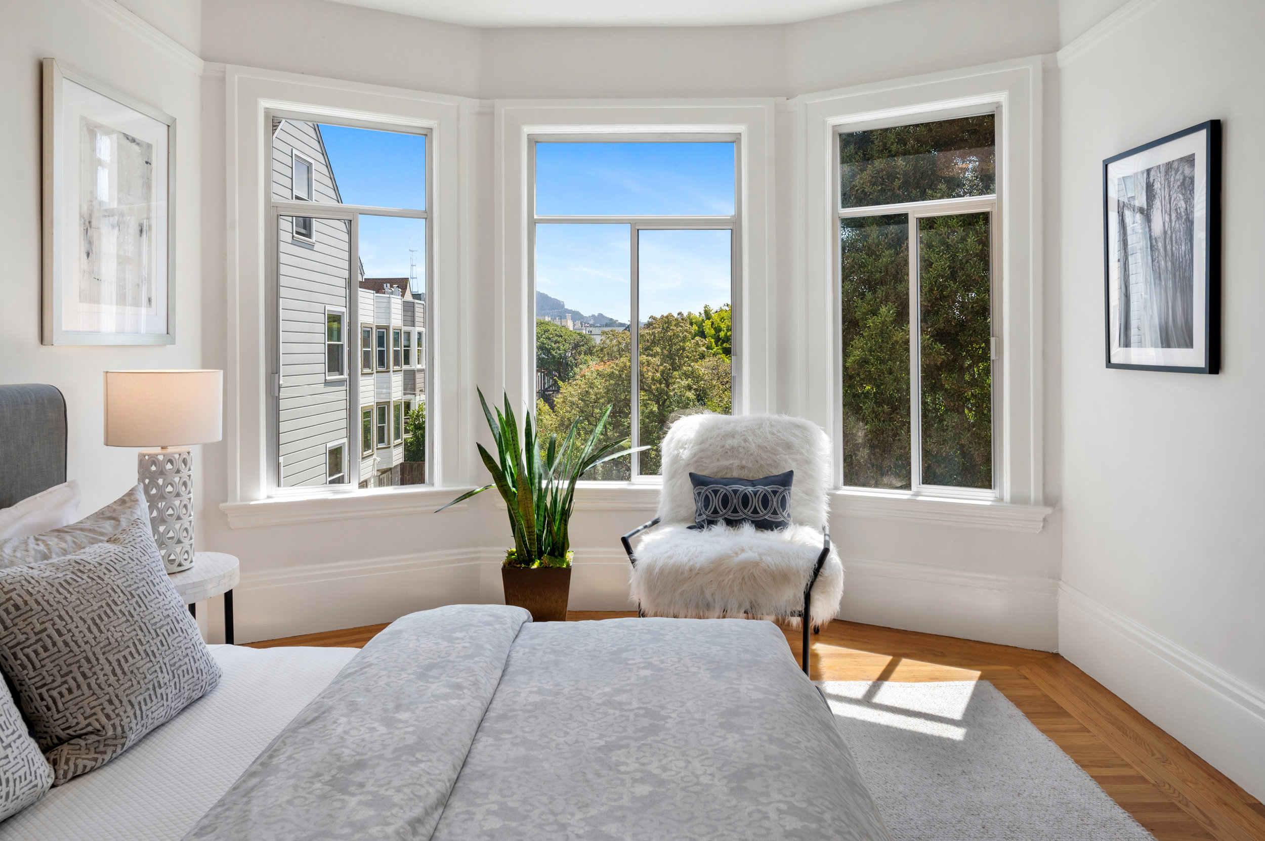 Close-up view of the second bedroom showing the large bay window with lush trees beyond