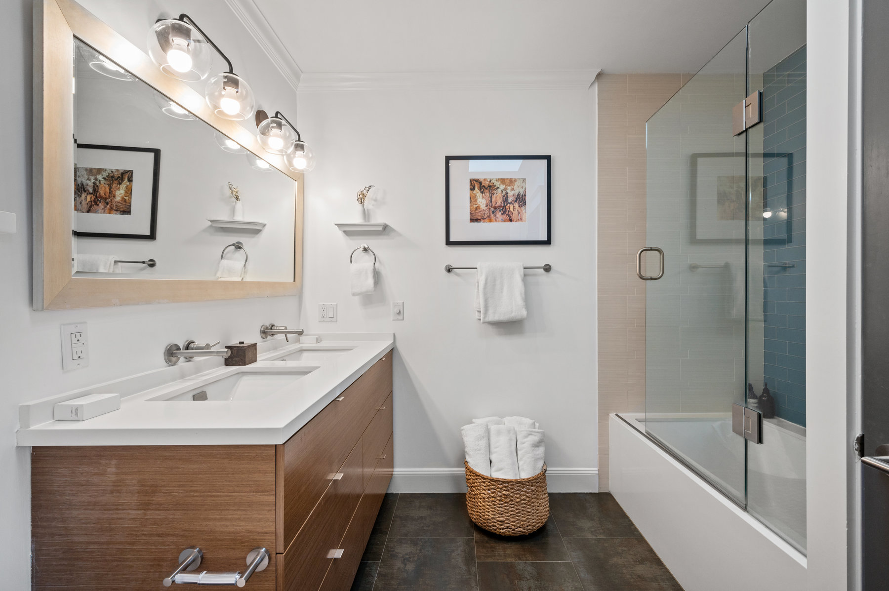 There is a large mirror above double vanity and shower/bath has large glass door.