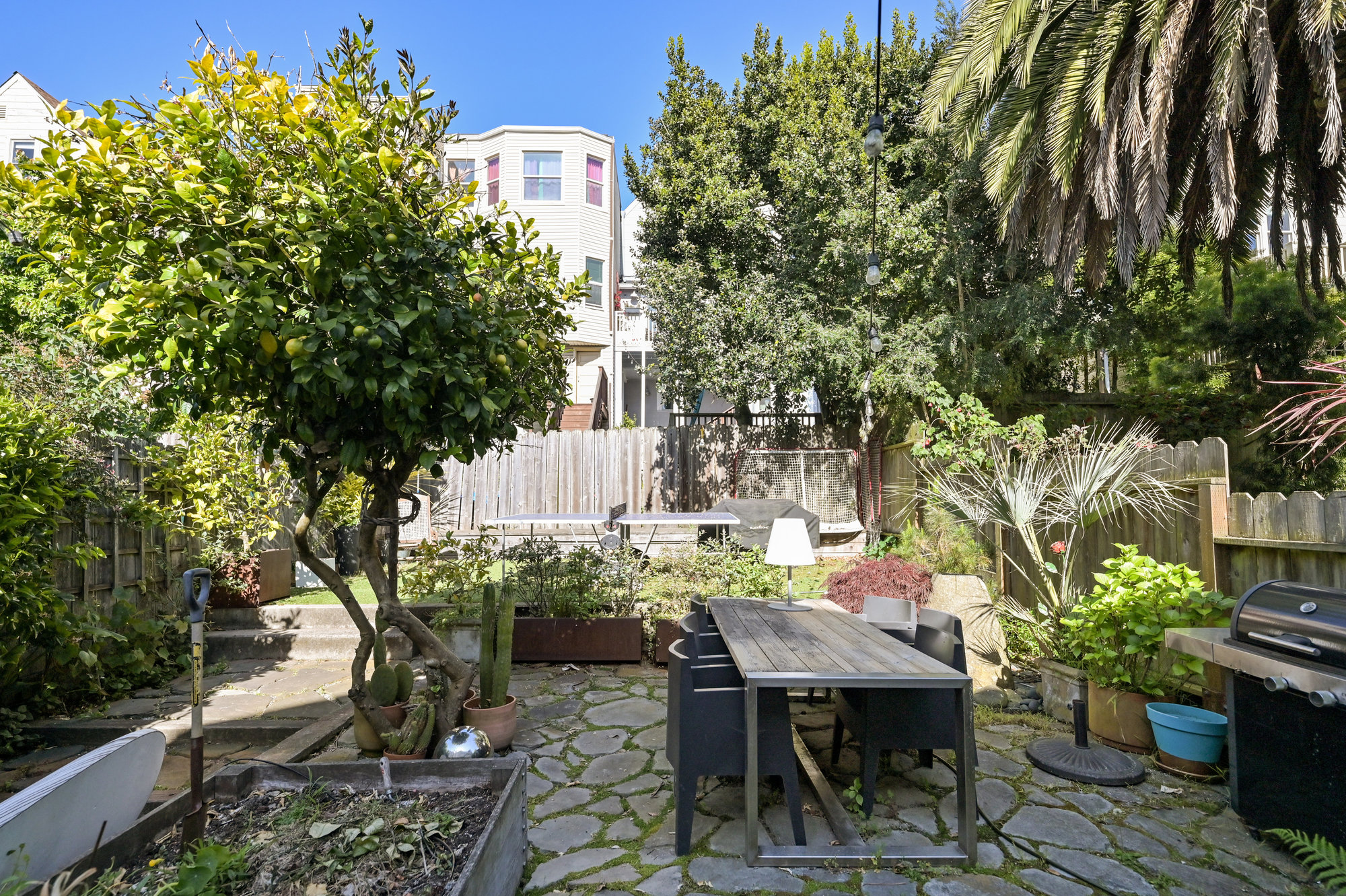 Long view of the yard, showing raised beds, trees, a wood fenced yard, and stone patio