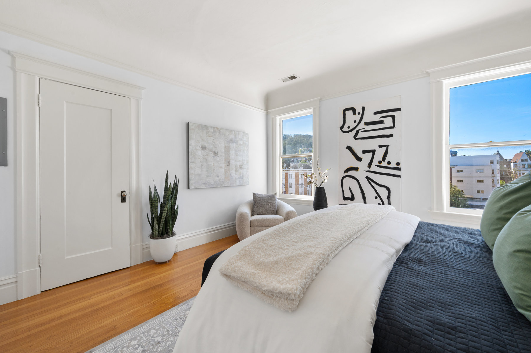 Primary bedroom has two large windows and hardwood floor throughout.