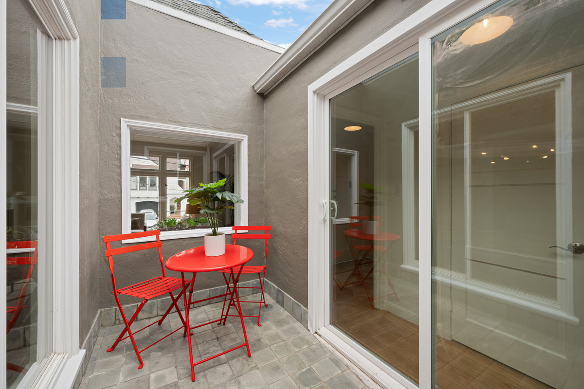 Center patio have cute red table and two chairs with tile floors.  There is a sliding glass door to the right.