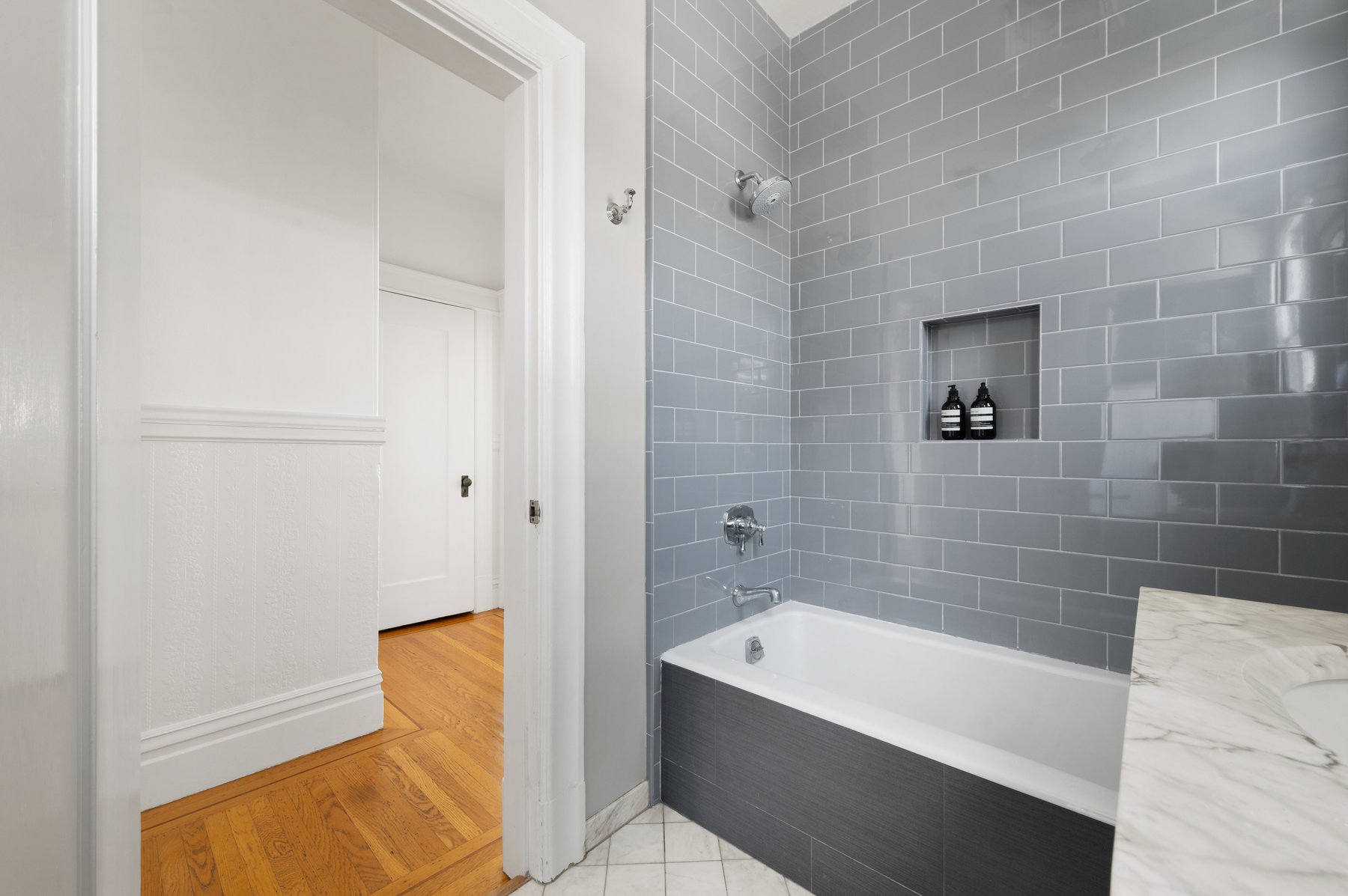 There is grey tile detail surrounding tub, and white tile floors. Bathroom has been updated.