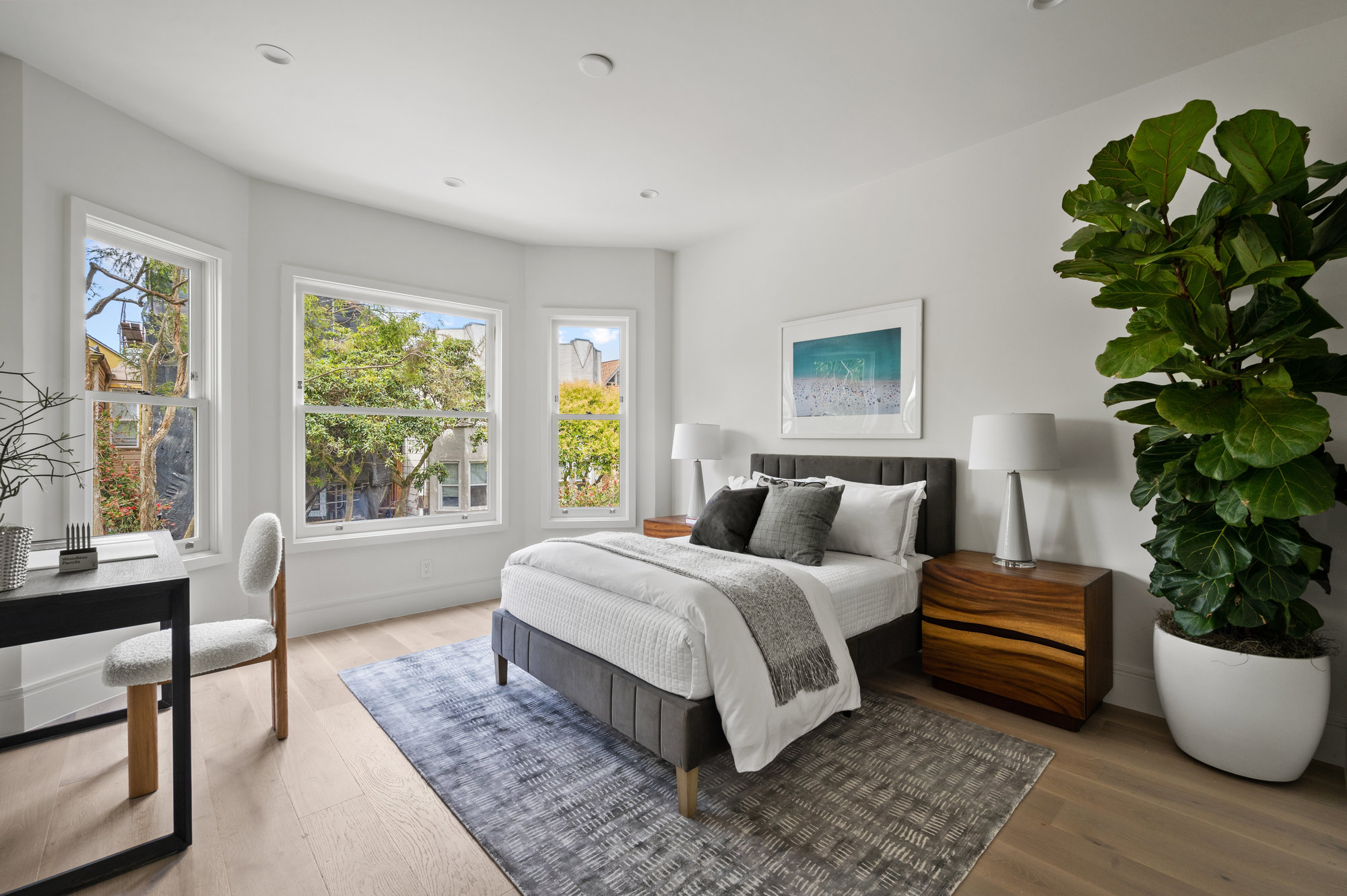 Guest bedroom has queen bed with two bedside tables and a small desk.  There are large bay windows.