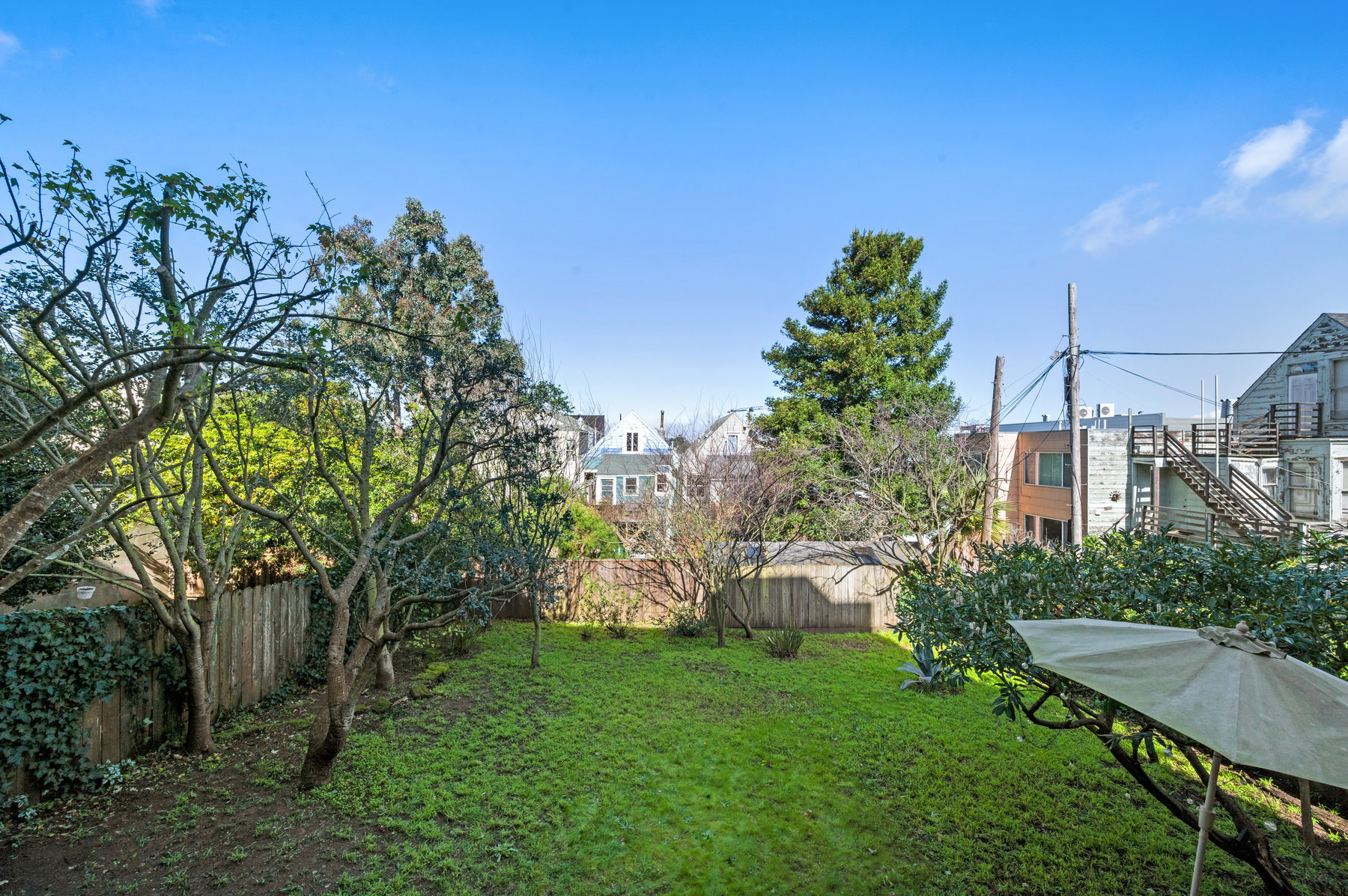 Yard is fenced in with sitting area to the right and has umbrella.