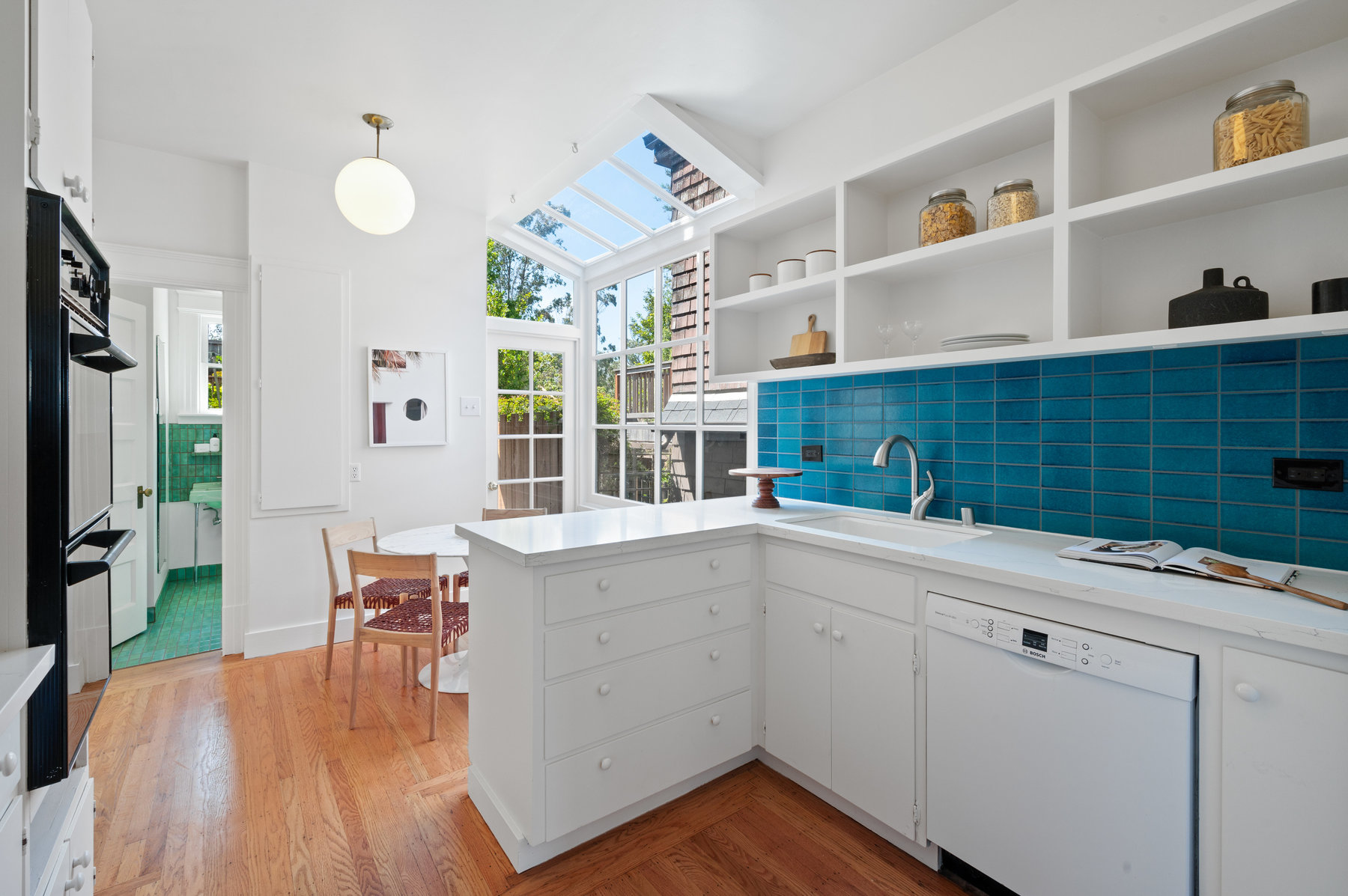 Kitchen has stunning teal Heath Tile backsplash with white counter top and cabinets.