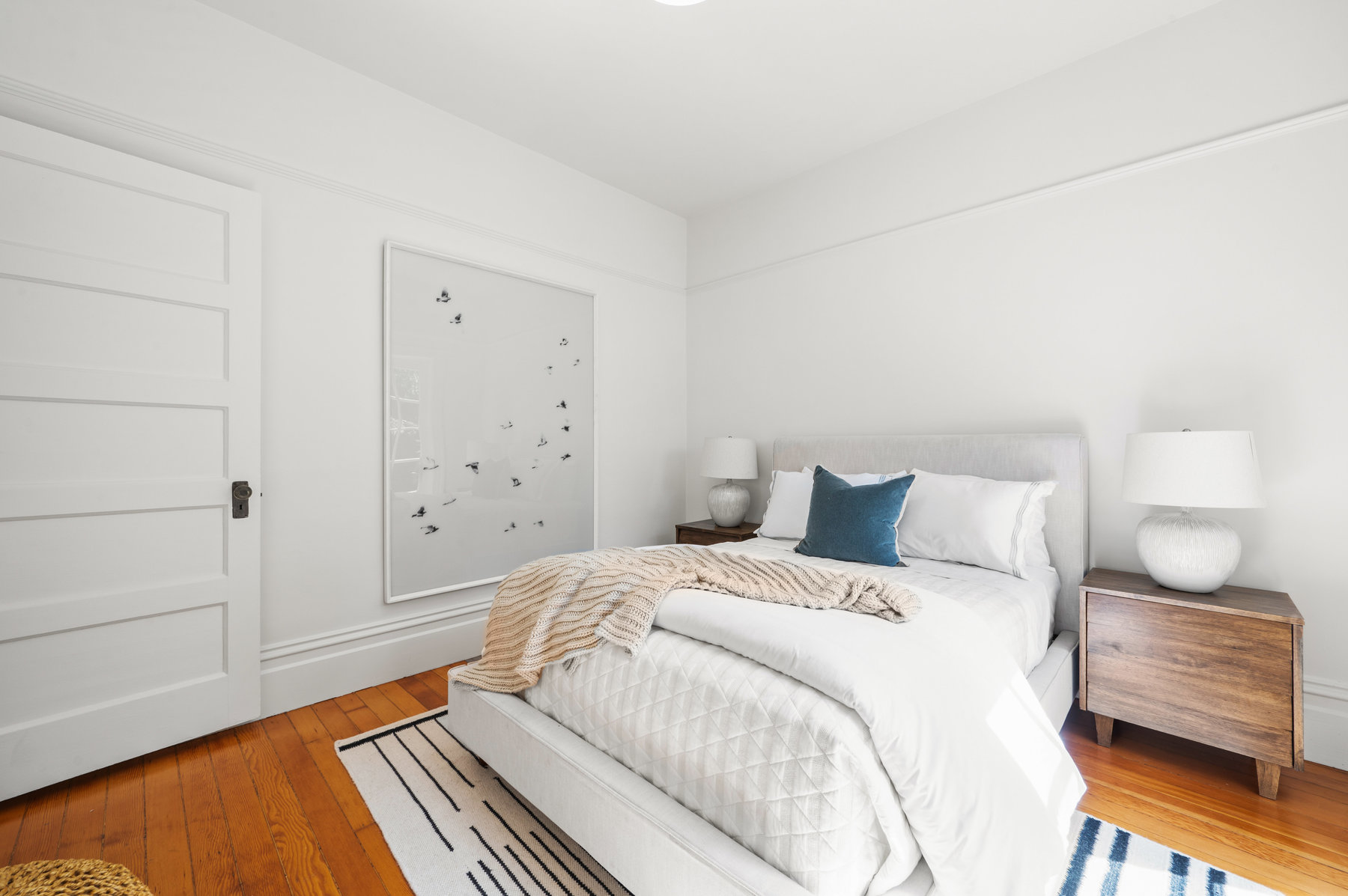 Back guest room has a queen sized bed with two bedside tables. Also has crown molding detail.