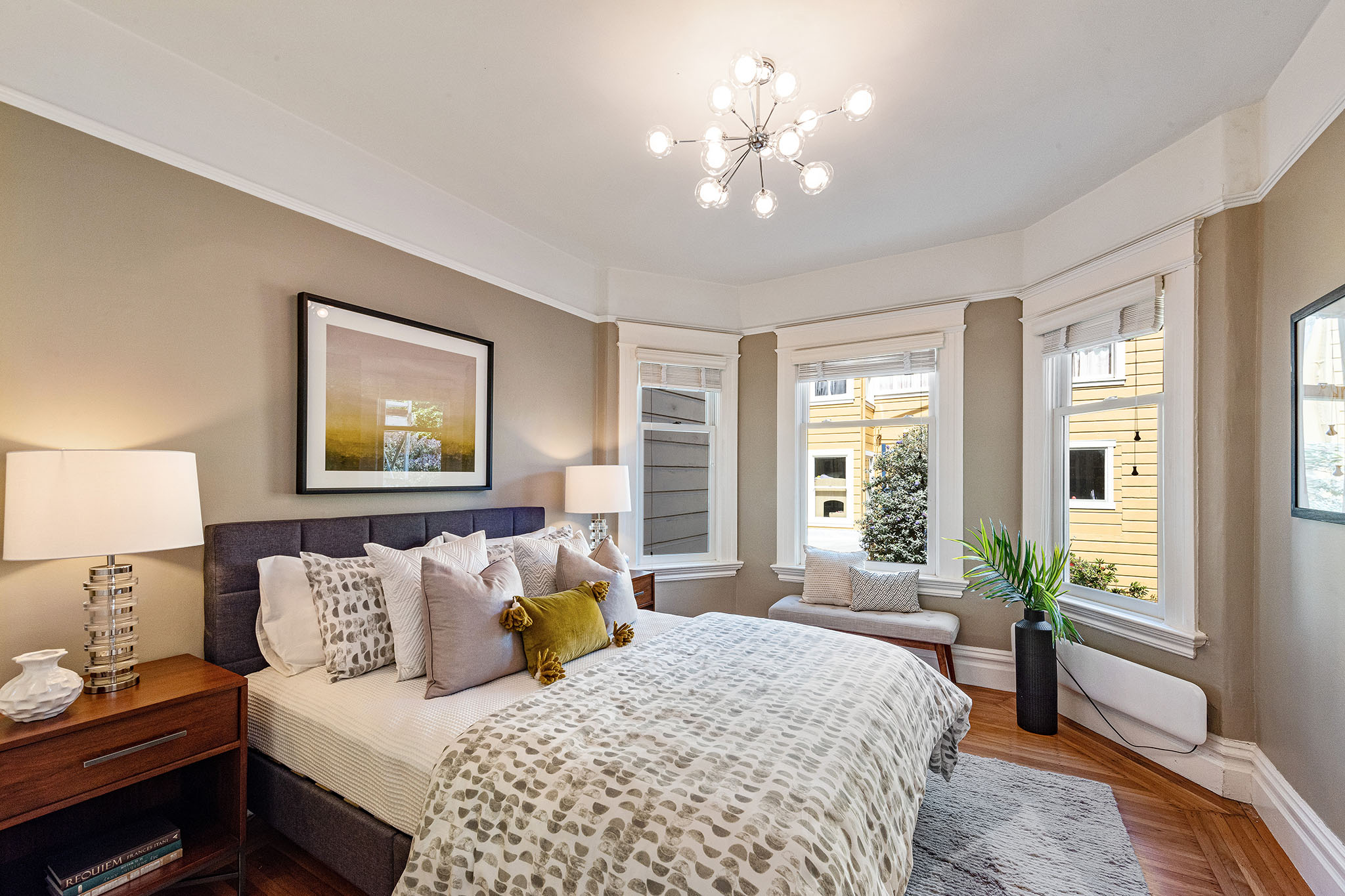 View of a large bedroom, showing three windows and wood floors