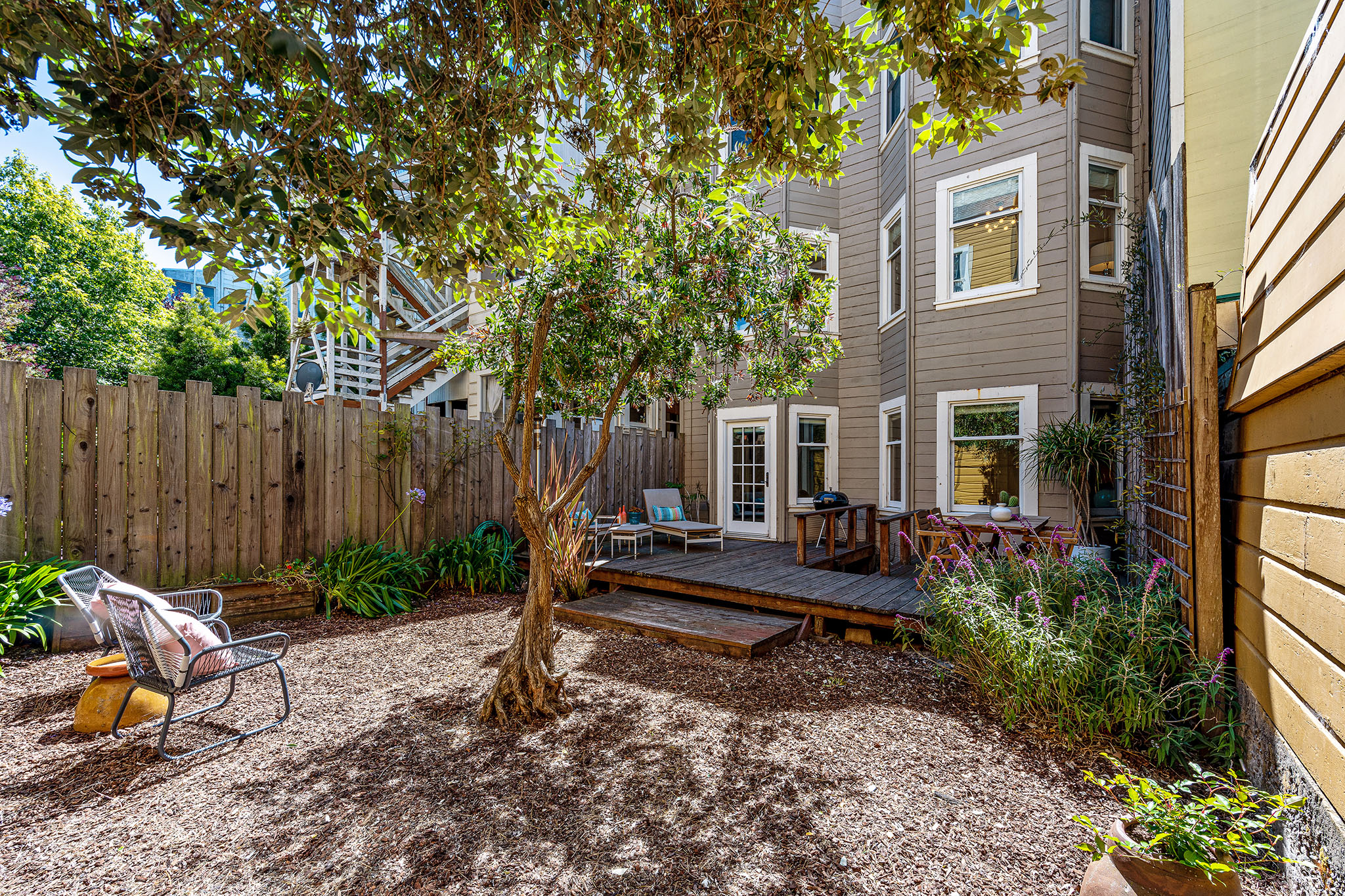 View of the rear yard, featuring trees and an outdoor seating area