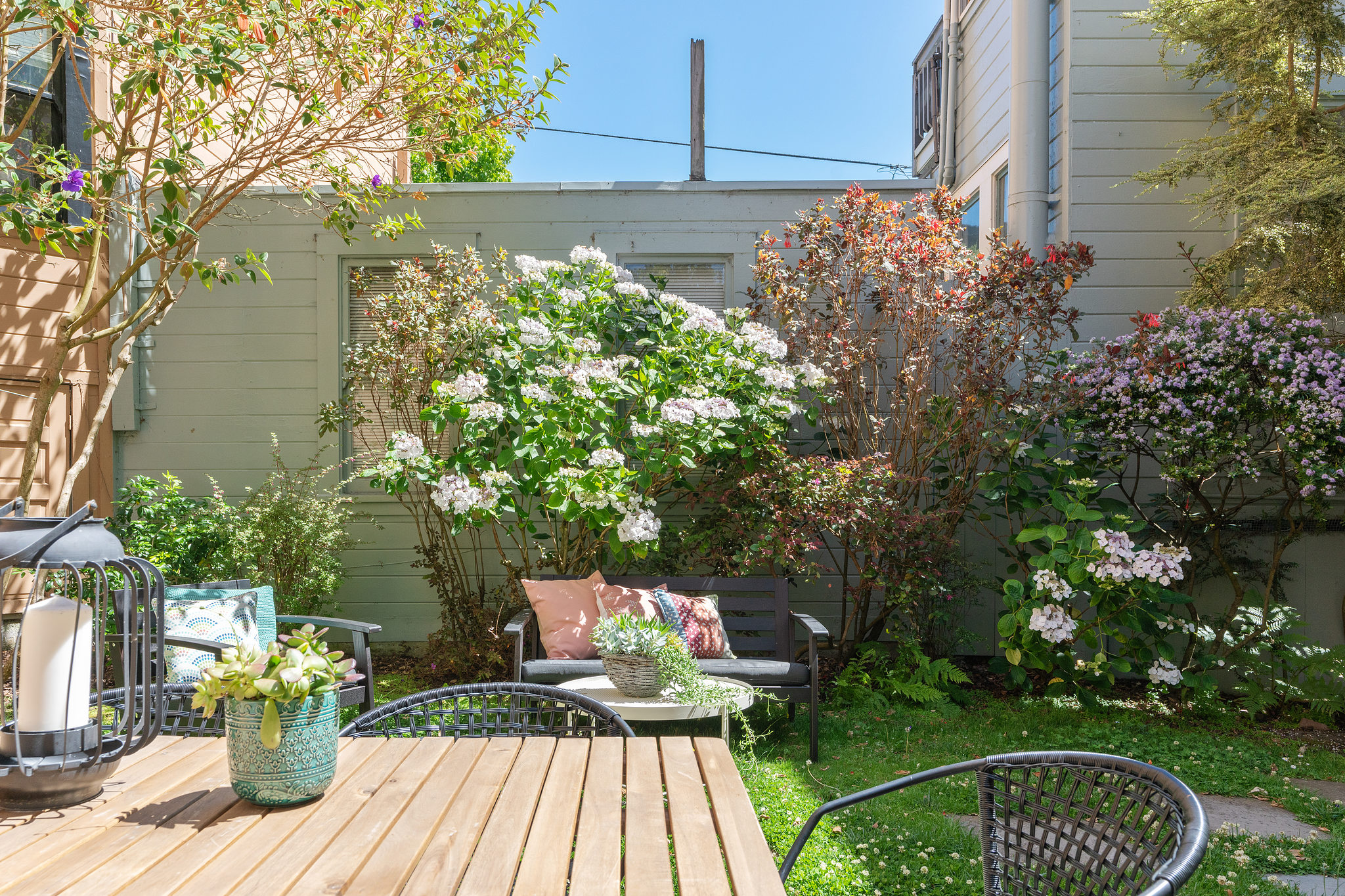View from the out door dining space, featuring lush plants and blooming bushes