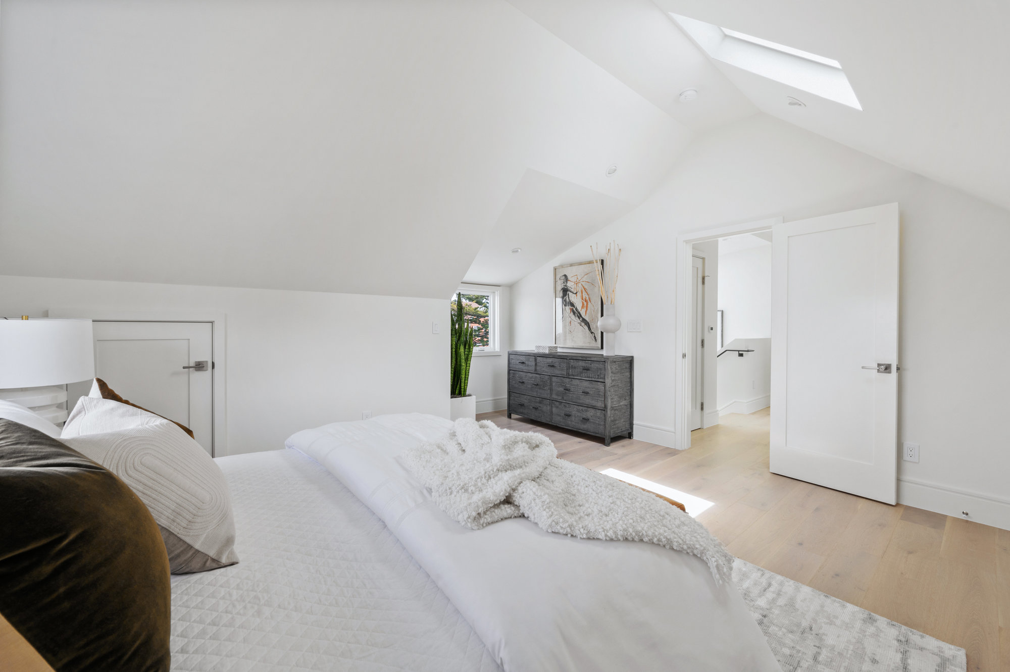 Looking over bed in primary to the doorway. There is a skylight.