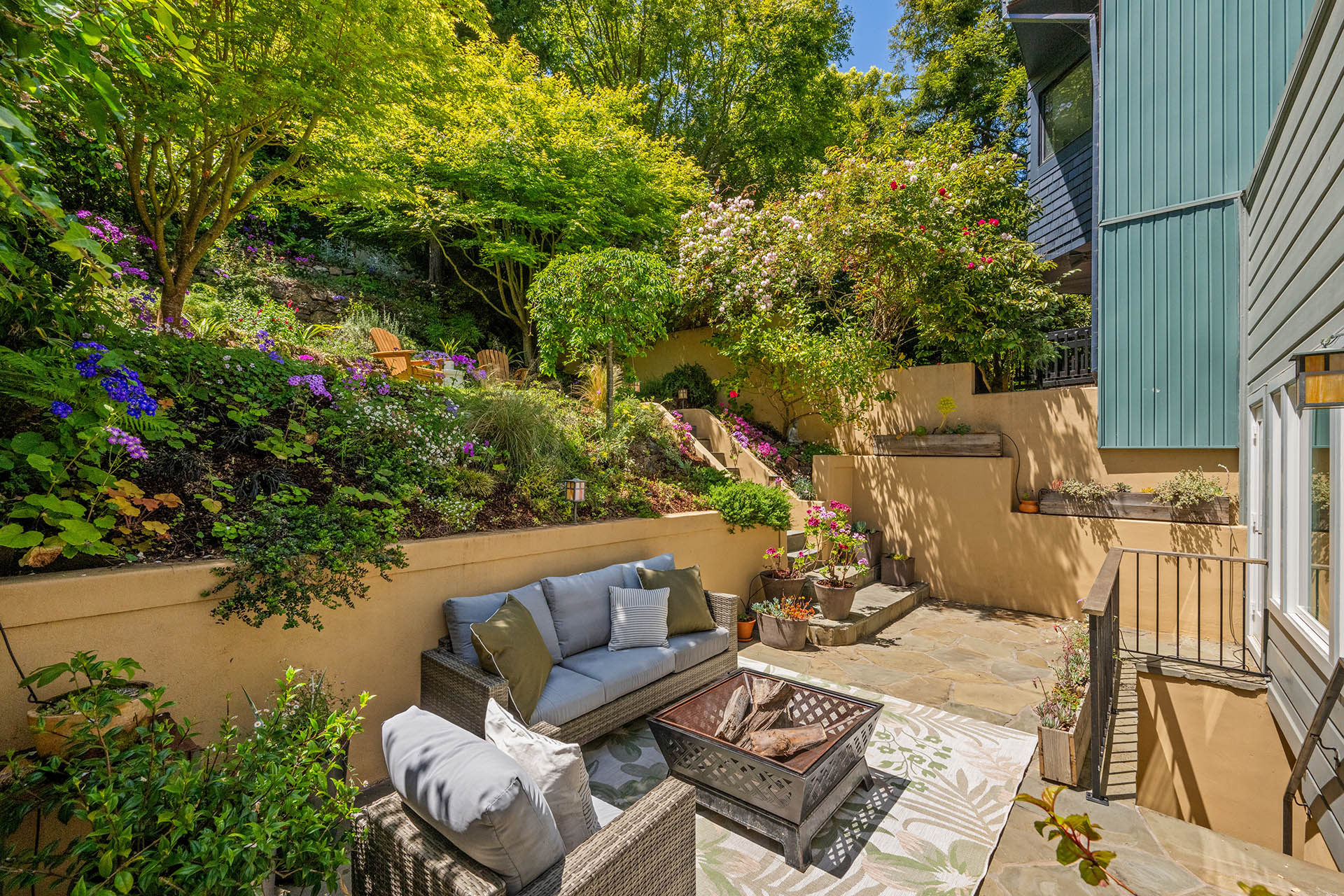 1525willard-garden-seating Backyard is on a hillside. There is a seating area and then lots of lush plants and flowers on the hillside.