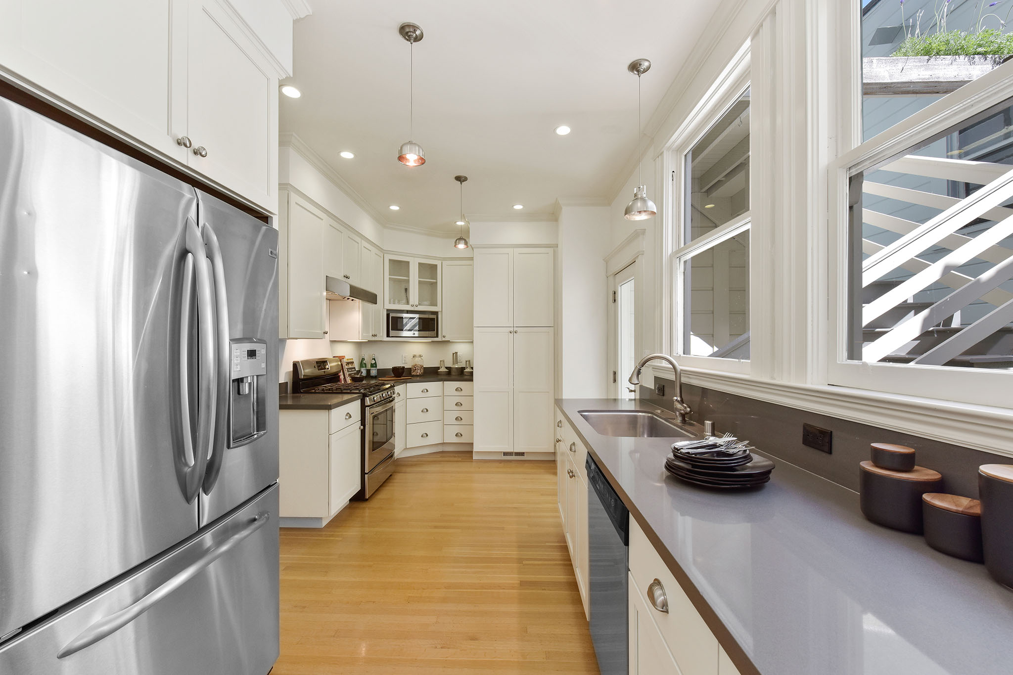 View of the kitchen, showing wood floors and windows above the sink and counters