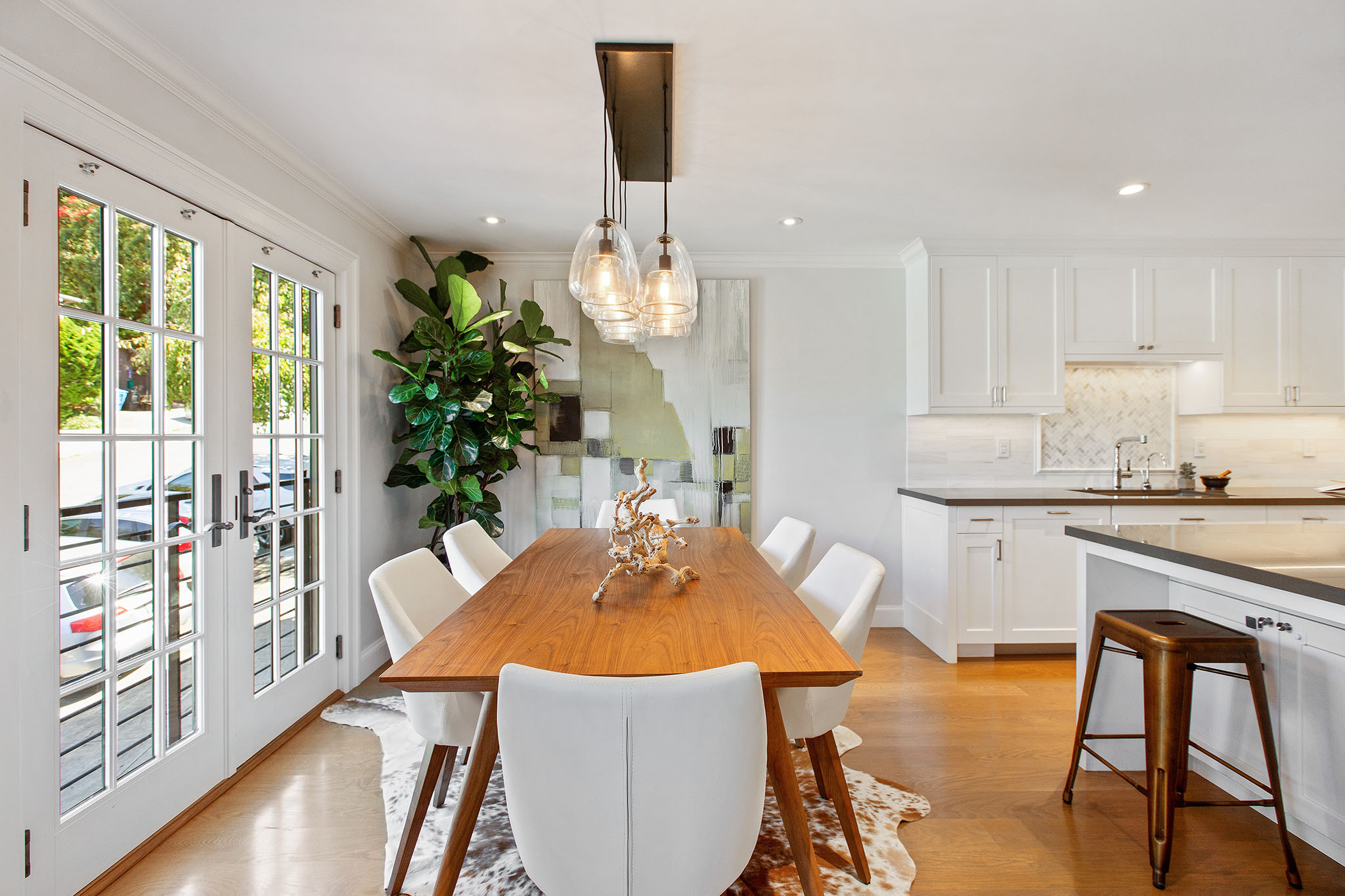 Looking over dining room table from living room. There is a large dining table that seats six. Glass french doors the left and kitchen is the right.