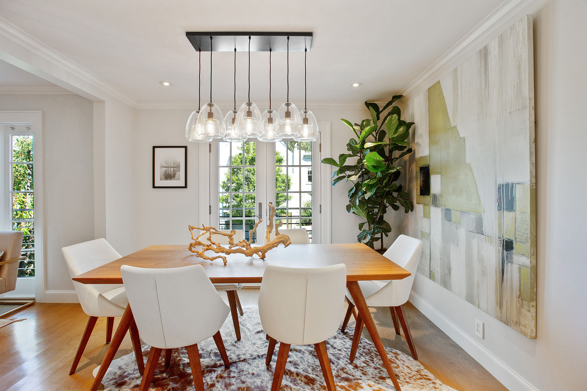 Centered photo of dining table. There is a modern glass light fixture above dining table.