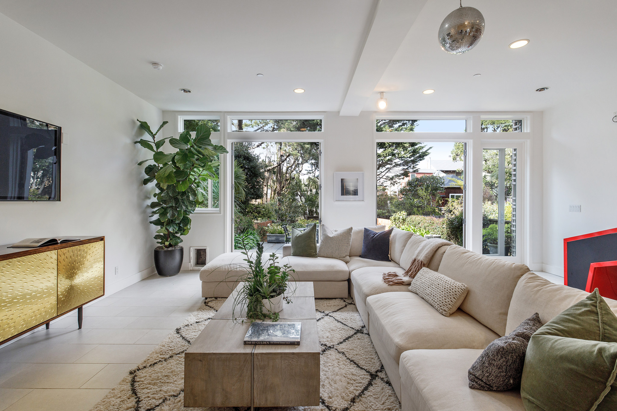 View of lower living area, with glass doors open showing the lush landscape beyond