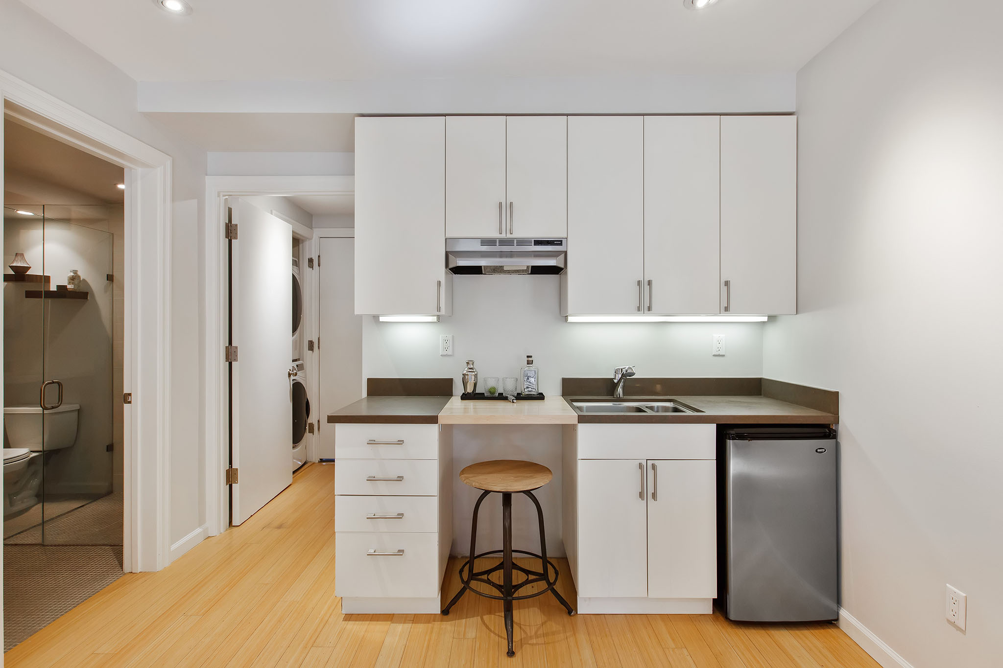 Centered photo of wet bar. There are upper and lower white cabinets.