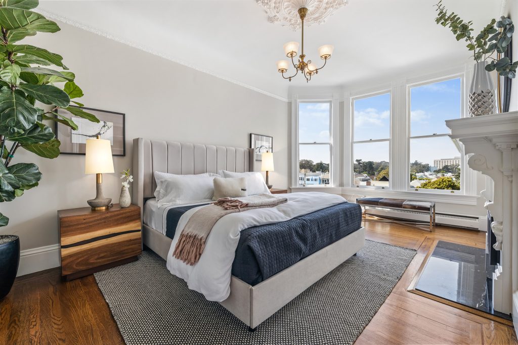 A large bedroom featuring three windows, a bed, rug, and table