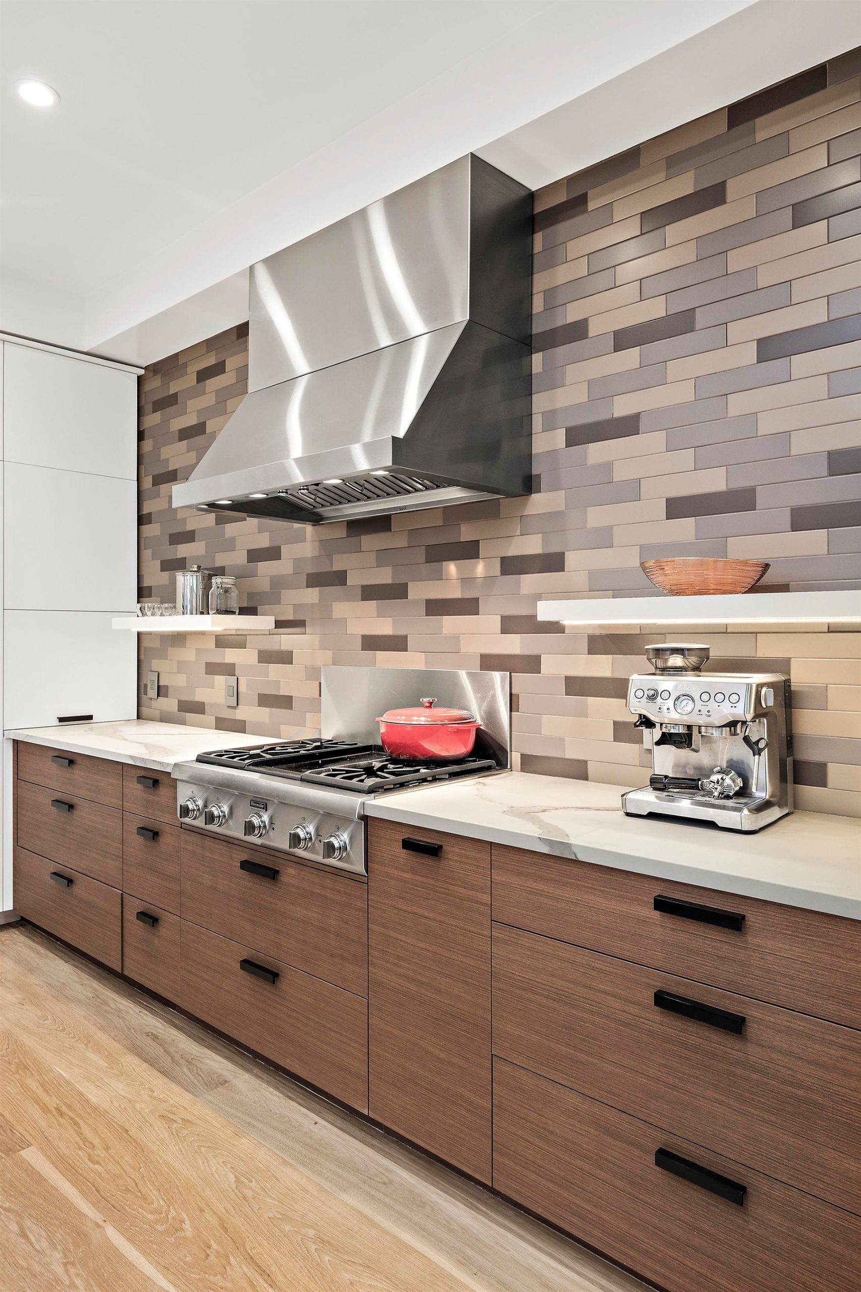 Gas stove is centered on back wall with with large stainless hood and tile backsplash detail.