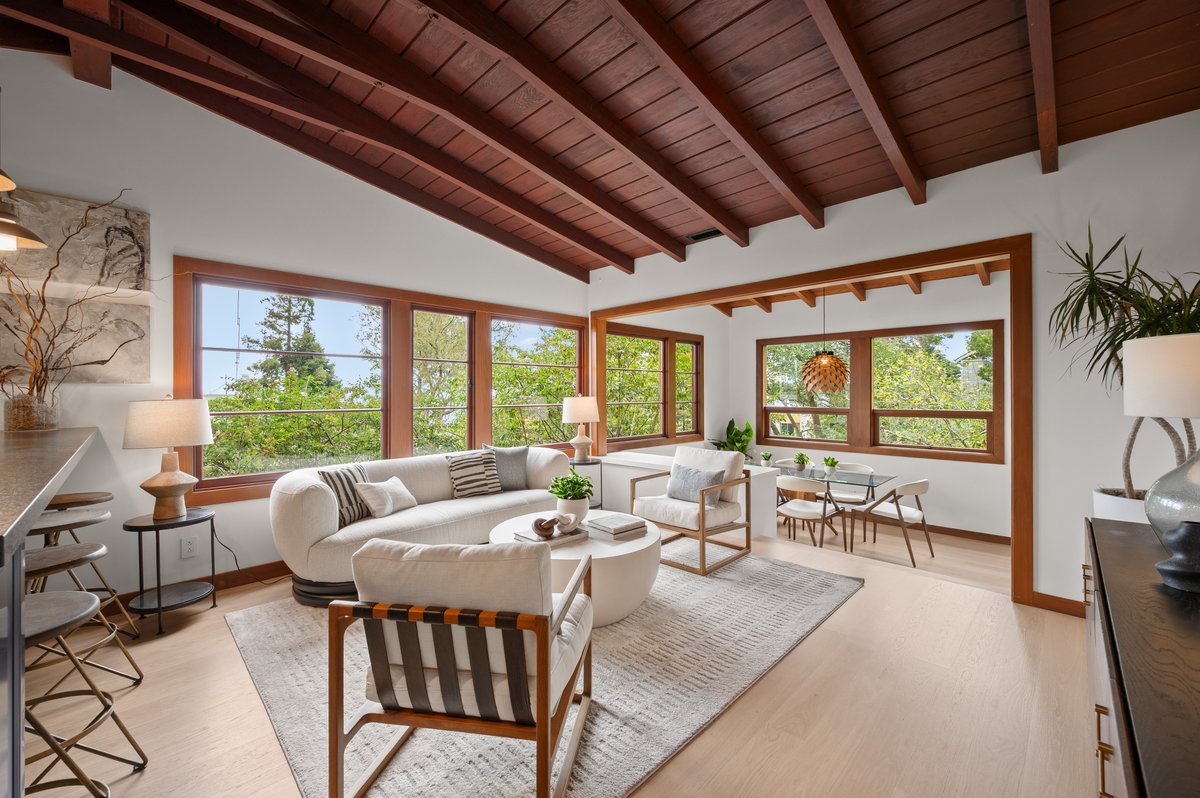 Bright living and dining area with large windows, white walls, wood ceiling, modern furniture, and light wood flooring surrounded by greenery outside. Bright living and dining area with large windows, white walls, wood ceiling, modern furniture, and light wood flooring surrounded by greenery outside.