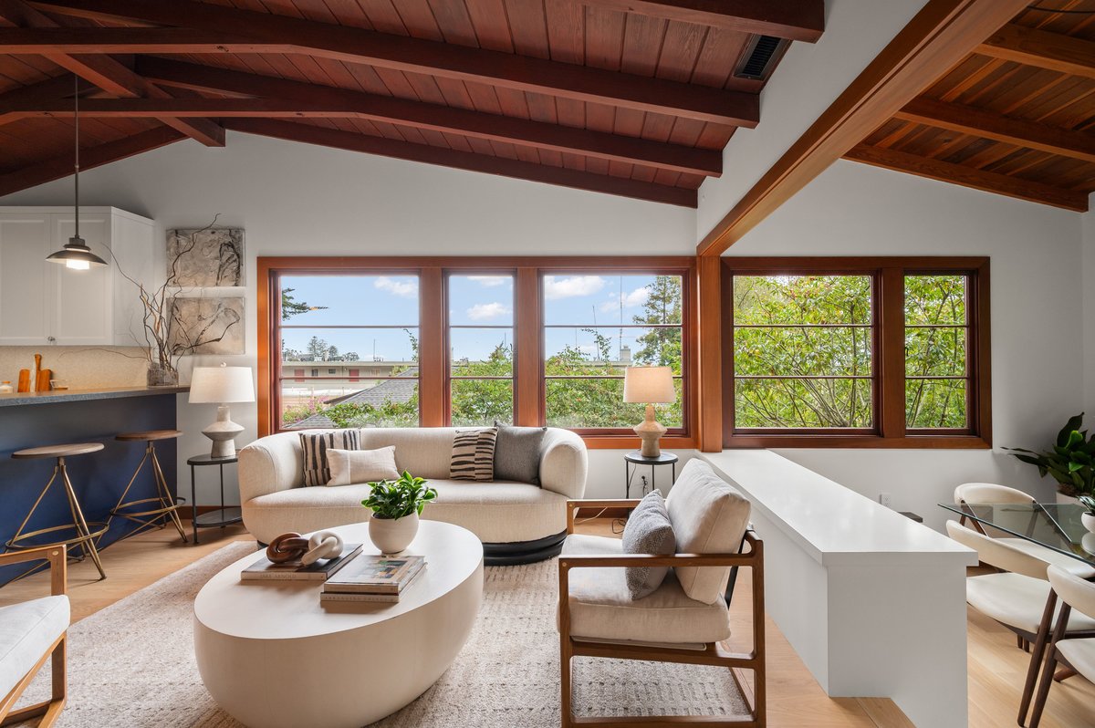 Living room with wood ceiling, large windows, neutral furniture, a round coffee table, and indoor plants, with a view of trees and sky outside. Living room with wood ceiling, large windows, neutral furniture, a round coffee table, and indoor plants, with a view of trees and sky outside.