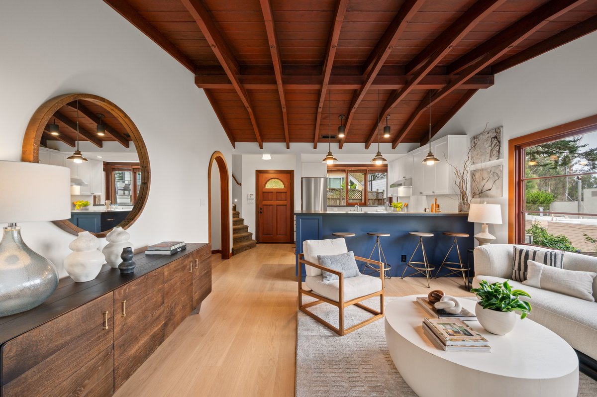 Modern open-concept living room and kitchen with wood ceiling, neutral furniture, blue kitchen island, and large windows letting in natural light. Modern open-concept living room and kitchen with wood ceiling, neutral furniture, blue kitchen island, and large windows letting in natural light.