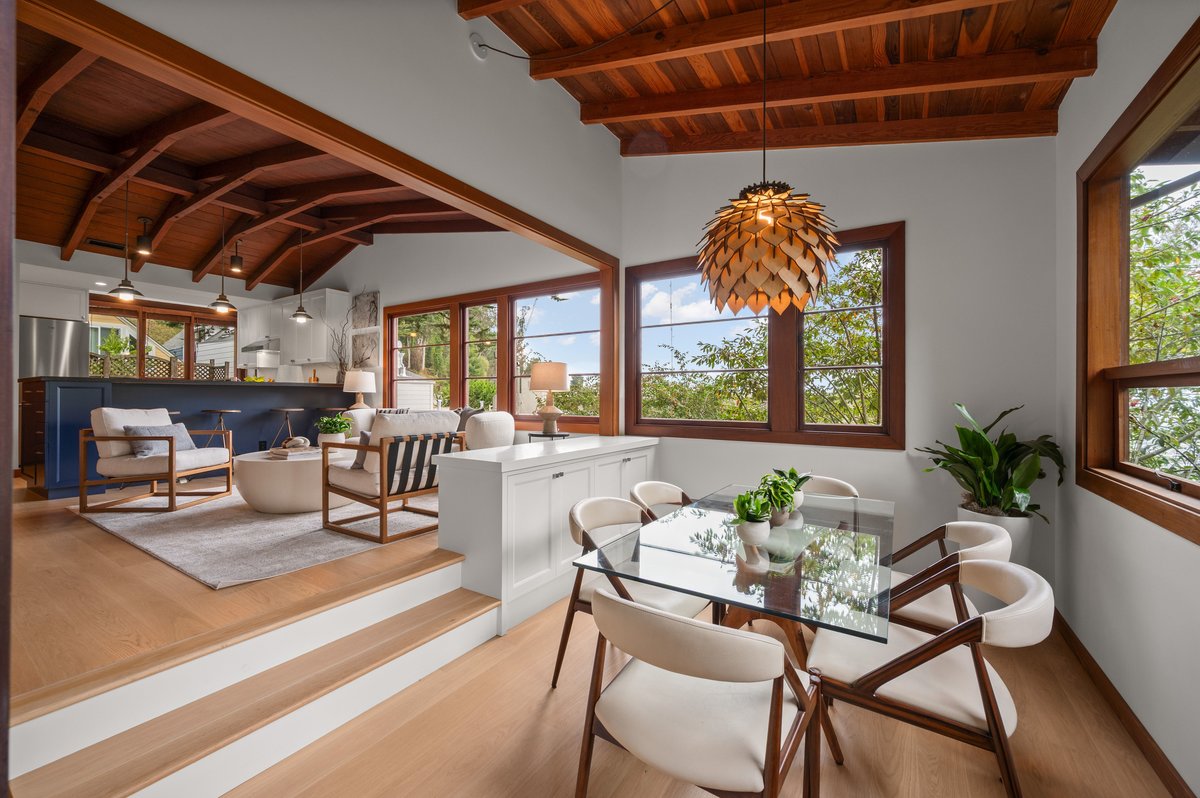 Open-concept living and dining area with wooden ceilings, modern furniture, glass dining table, large windows, and indoor plants. Open-concept living and dining area with wooden ceilings, modern furniture, glass dining table, large windows, and indoor plants.