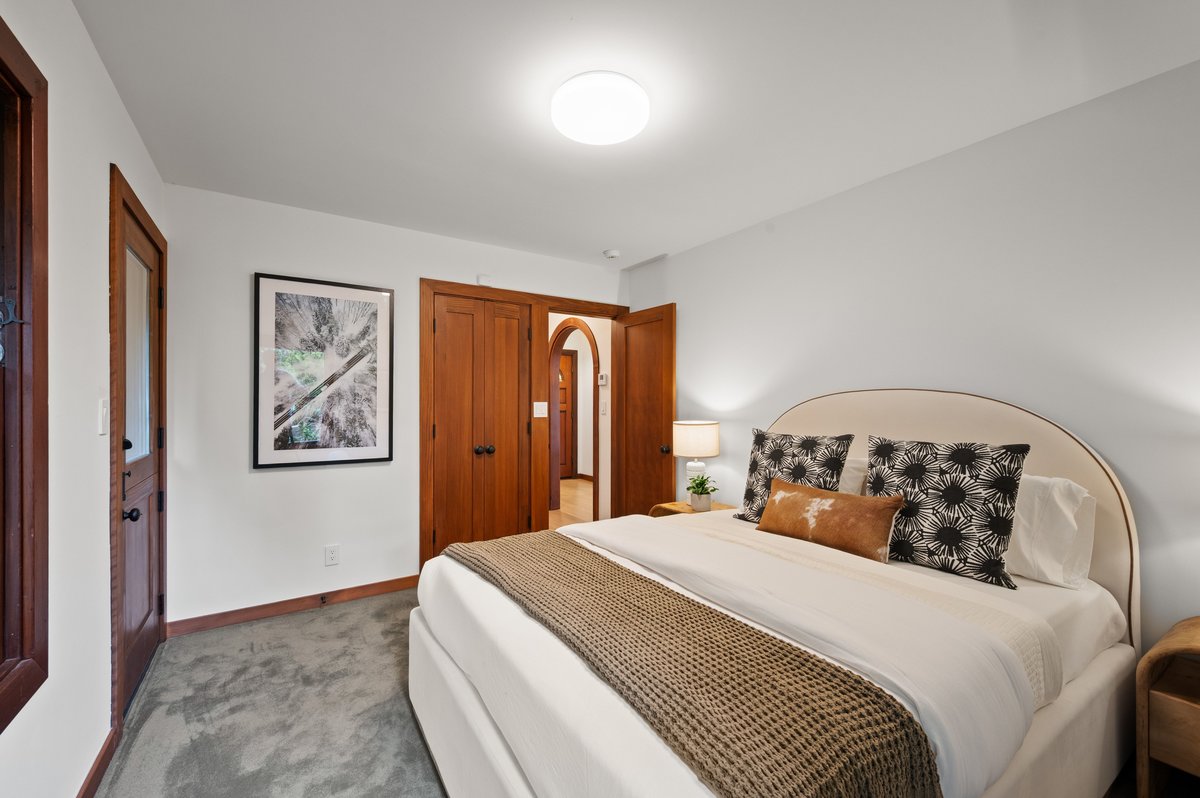 Bedroom with a neatly made bed, two patterned pillows, a bed throw, a nightstand with a lamp, wooden doors, and a framed nature picture on a white wall. Bedroom with a neatly made bed, two patterned pillows, a bed throw, a nightstand with a lamp, wooden doors, and a framed nature picture on a white wall.