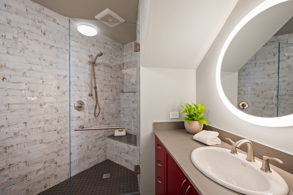 Modern bathroom with a walk-in shower, glass door, handheld showerhead, vanity with round mirror, sink, faucet, and a potted plant on the countertop. Modern bathroom with a walk-in shower, glass door, handheld showerhead, vanity with round mirror, sink, faucet, and a potted plant on the countertop.