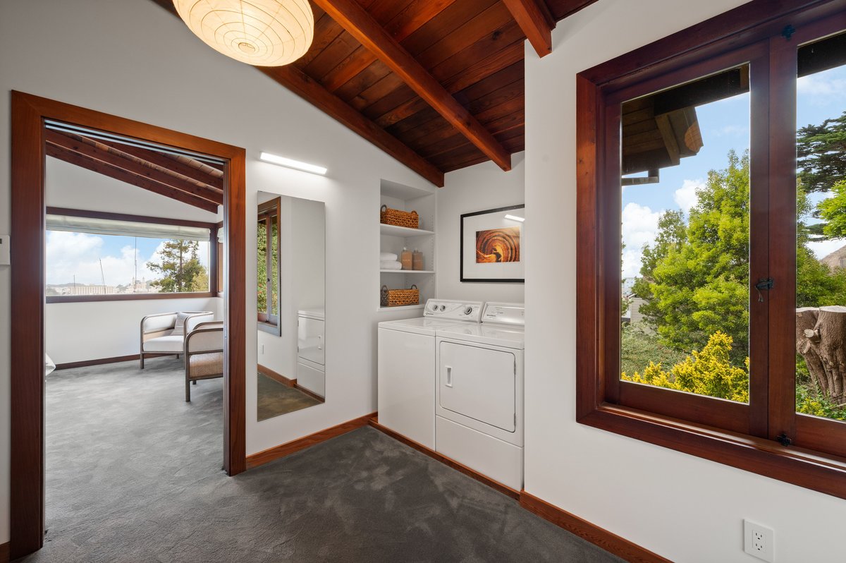 Compact laundry area with a washer and dryer is built into a hallway nook; large windows and a mirror reflect natural light from an adjoining bedroom. Compact laundry area with a washer and dryer is built into a hallway nook; large windows and a mirror reflect natural light from an adjoining bedroom.