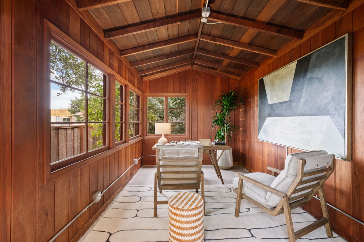Home office with wood-paneled walls, windows, a desk with a lamp, two chairs, a plant, abstract art, and a patterned rug. Home office with wood-paneled walls, windows, a desk with a lamp, two chairs, a plant, abstract art, and a patterned rug.