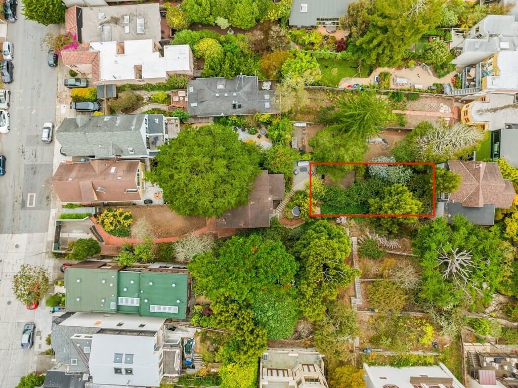 Aerial view of a residential neighborhood with trees and houses; a rectangular plot of land is outlined in red near the center-right of the image. Aerial view of a residential neighborhood with trees and houses; a rectangular plot of land is outlined in red near the center-right of the image.