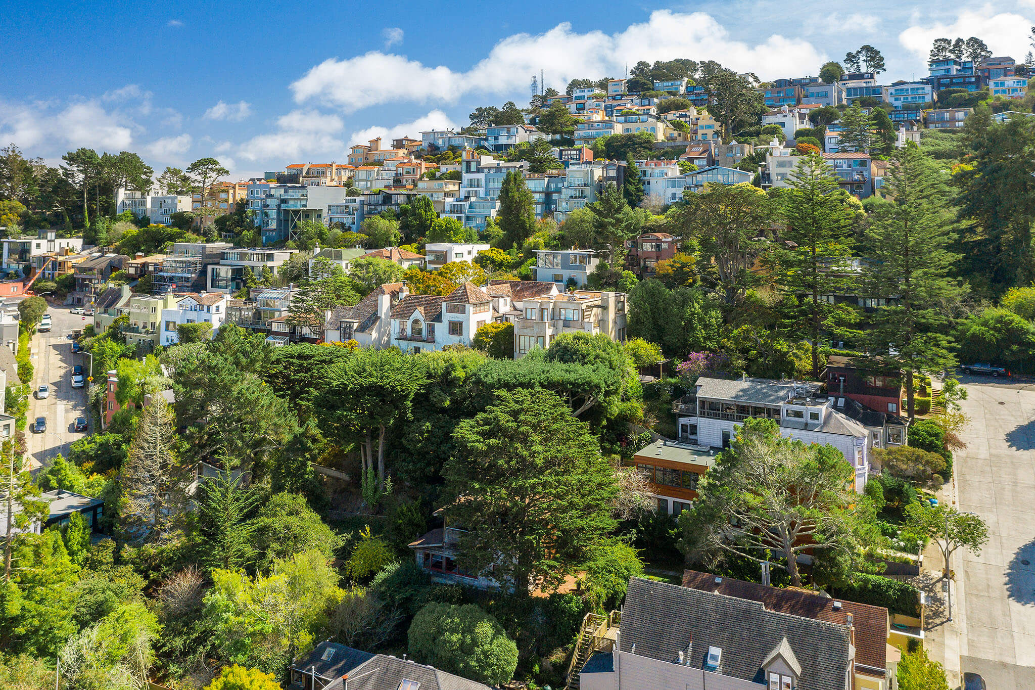 Hillside residential neighborhood with densely packed houses, lush green trees, and clear blue sky in the background. Hillside residential neighborhood with densely packed houses, lush green trees, and clear blue sky in the background.