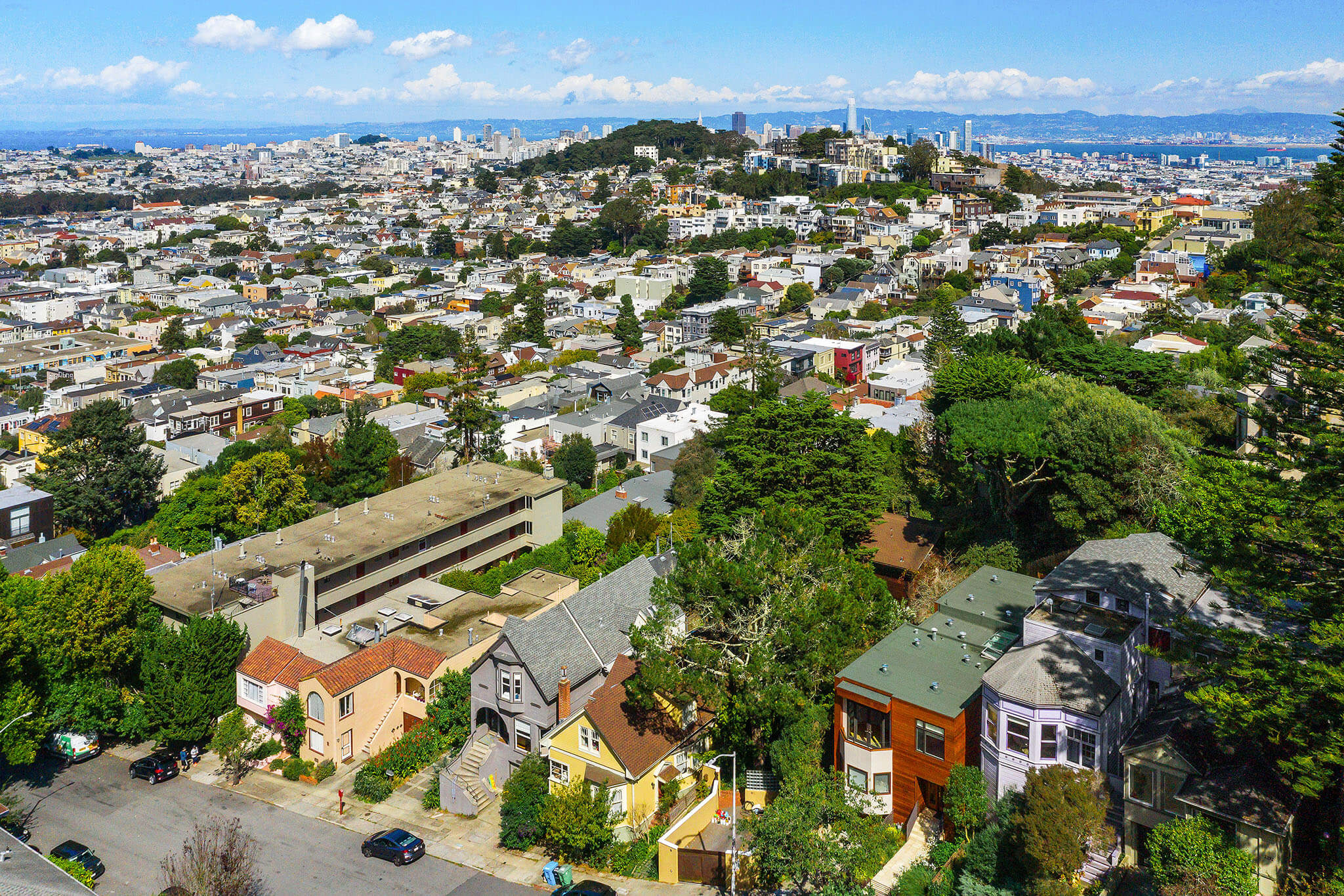 Aerial view of a residential neighborhood with houses, trees, and streets; cityscape and distant hills visible under a partly cloudy sky. Aerial view of a residential neighborhood with houses, trees, and streets; cityscape and distant hills visible under a partly cloudy sky.