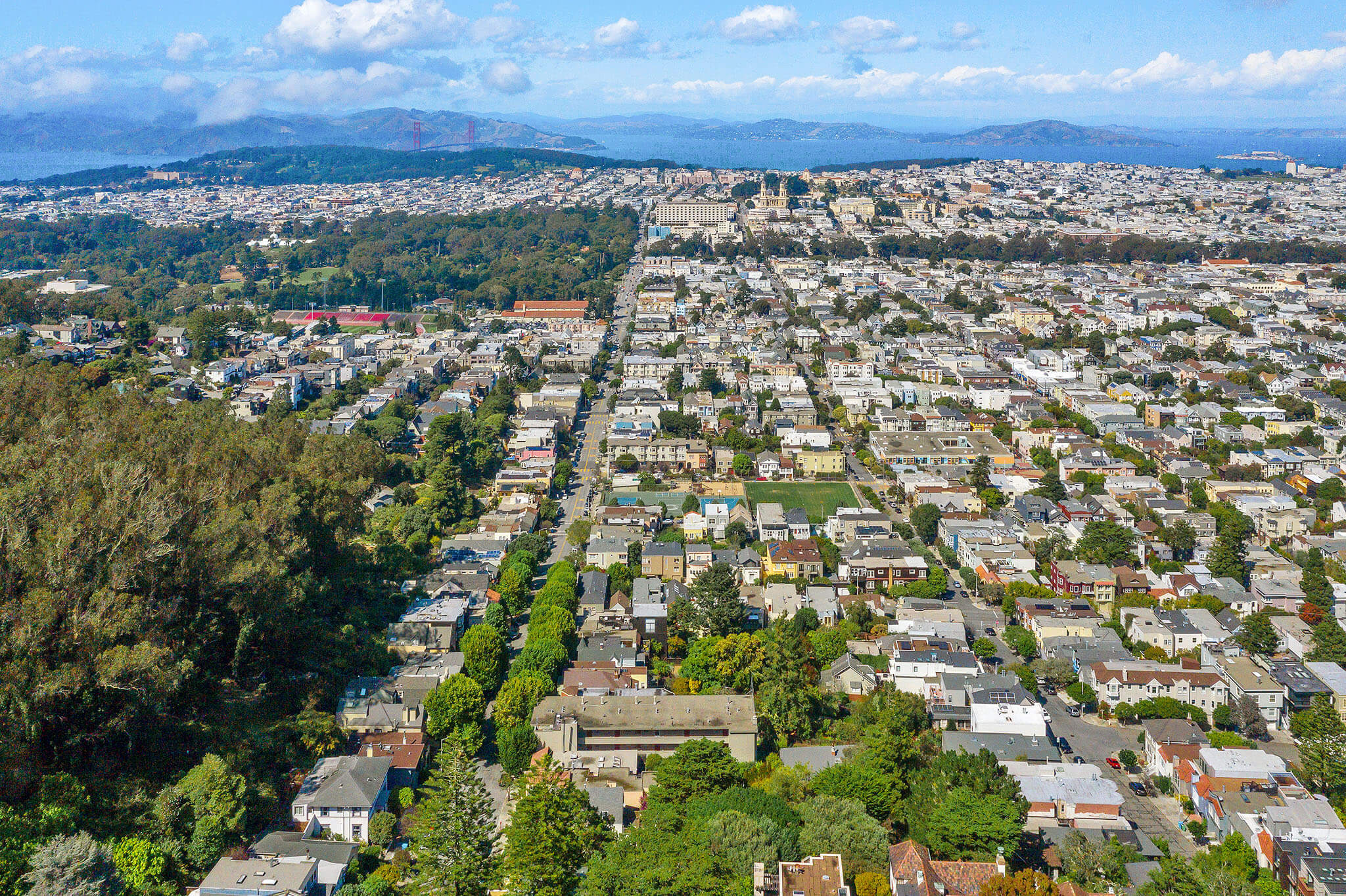 Aerial view of a residential neighborhood with grid streets, green spaces, and distant hills under a partly cloudy sky. Aerial view of a residential neighborhood with grid streets, green spaces, and distant hills under a partly cloudy sky.