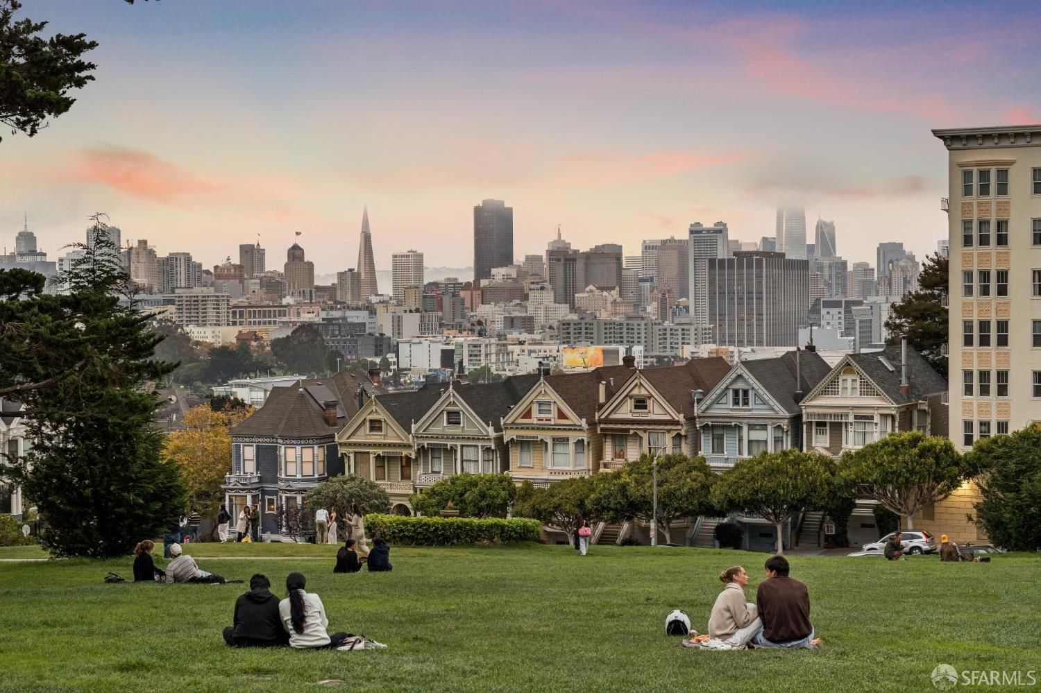 People sitting on the grass at Alamo Square Park with the Painted Ladies houses and the San Francisco skyline in the background. People sitting on the grass at Alamo Square Park with the Painted Ladies houses and the San Francisco skyline in the background.