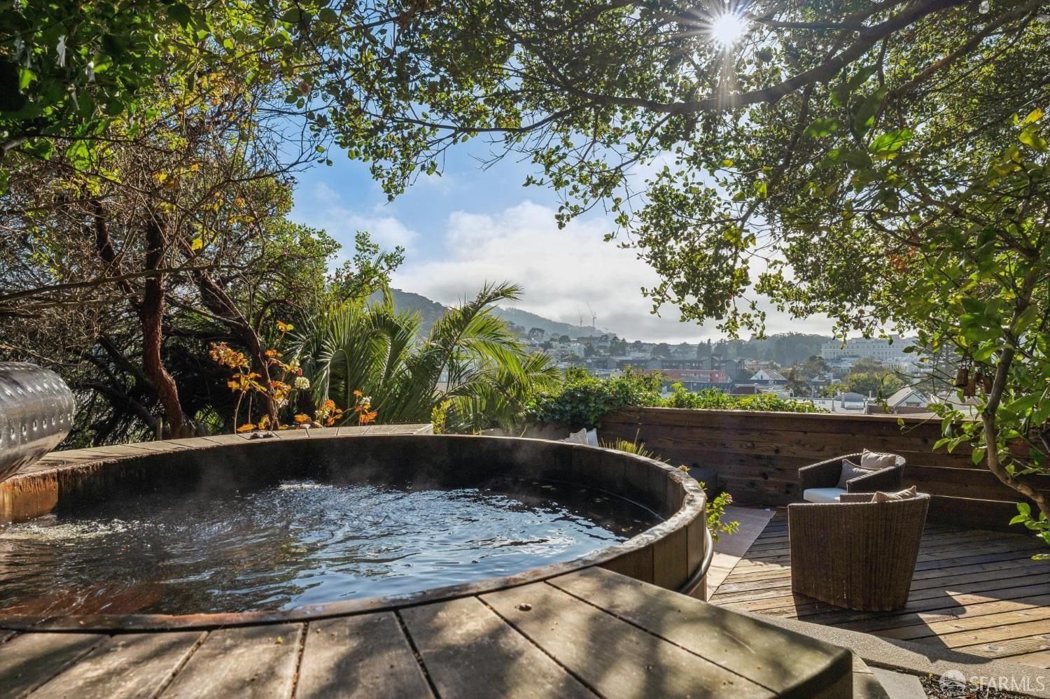 A round wooden hot tub on a deck overlooking a hillside city. A round wooden hot tub on a deck overlooking a hillside city.